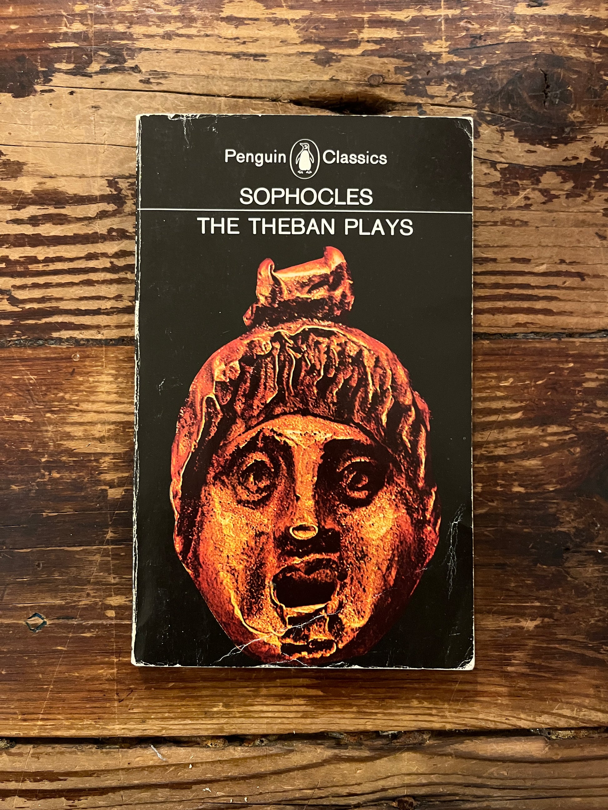 Book titled 'The Theban Plays' by Sophocles on a wooden surface