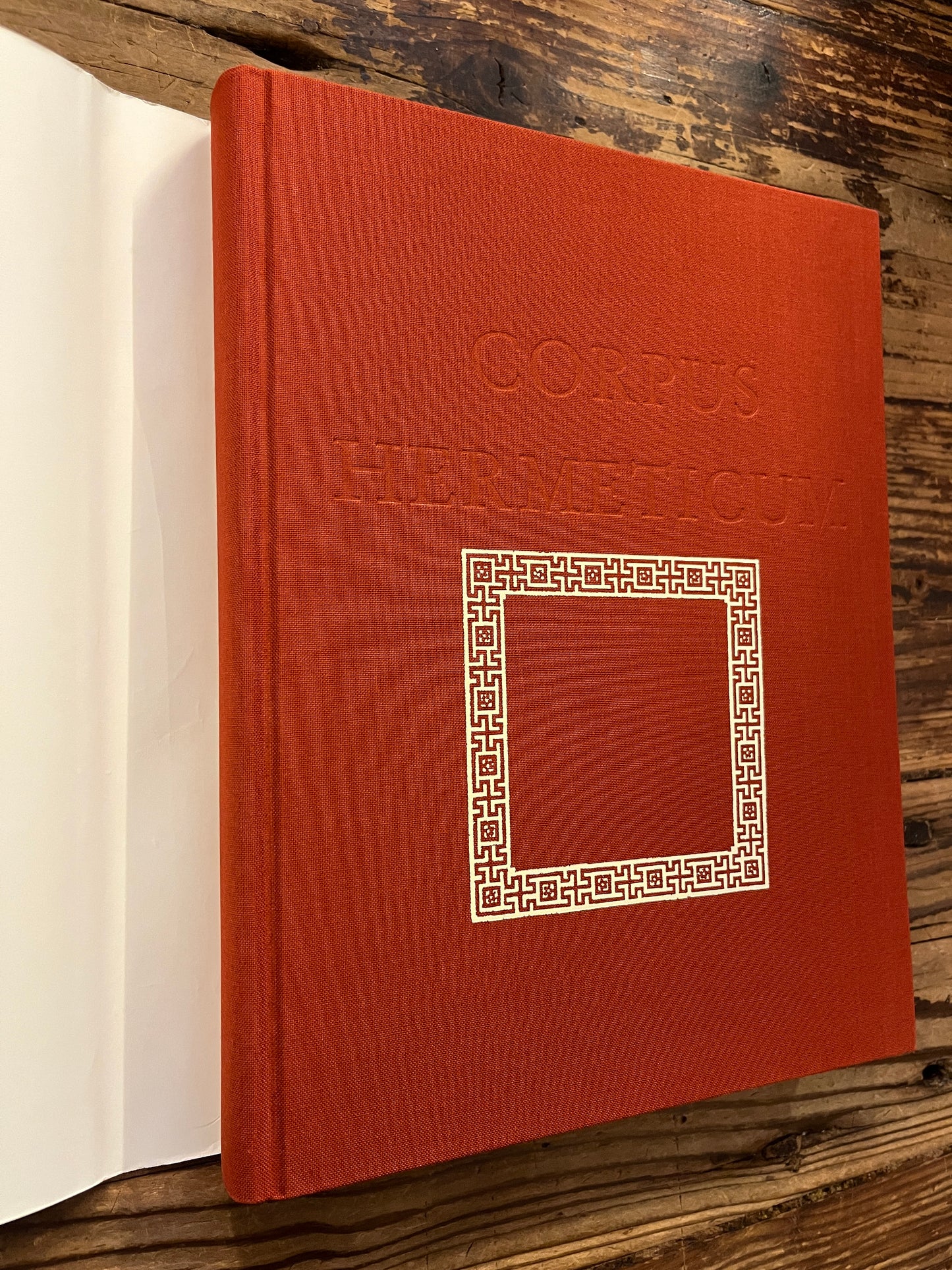 Voorkant zonder stof omslag van het boek 'Corpus hermeticum' ingeleid, vertaald en toegelicht door R. van den Broek en G. Quispel, op een houten achtergrond