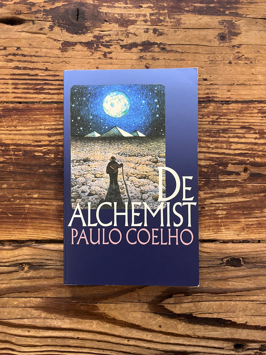 Voorkant van boek met de titel 'de Alchemist' door Paulo Coelho op een houten achtergrond 