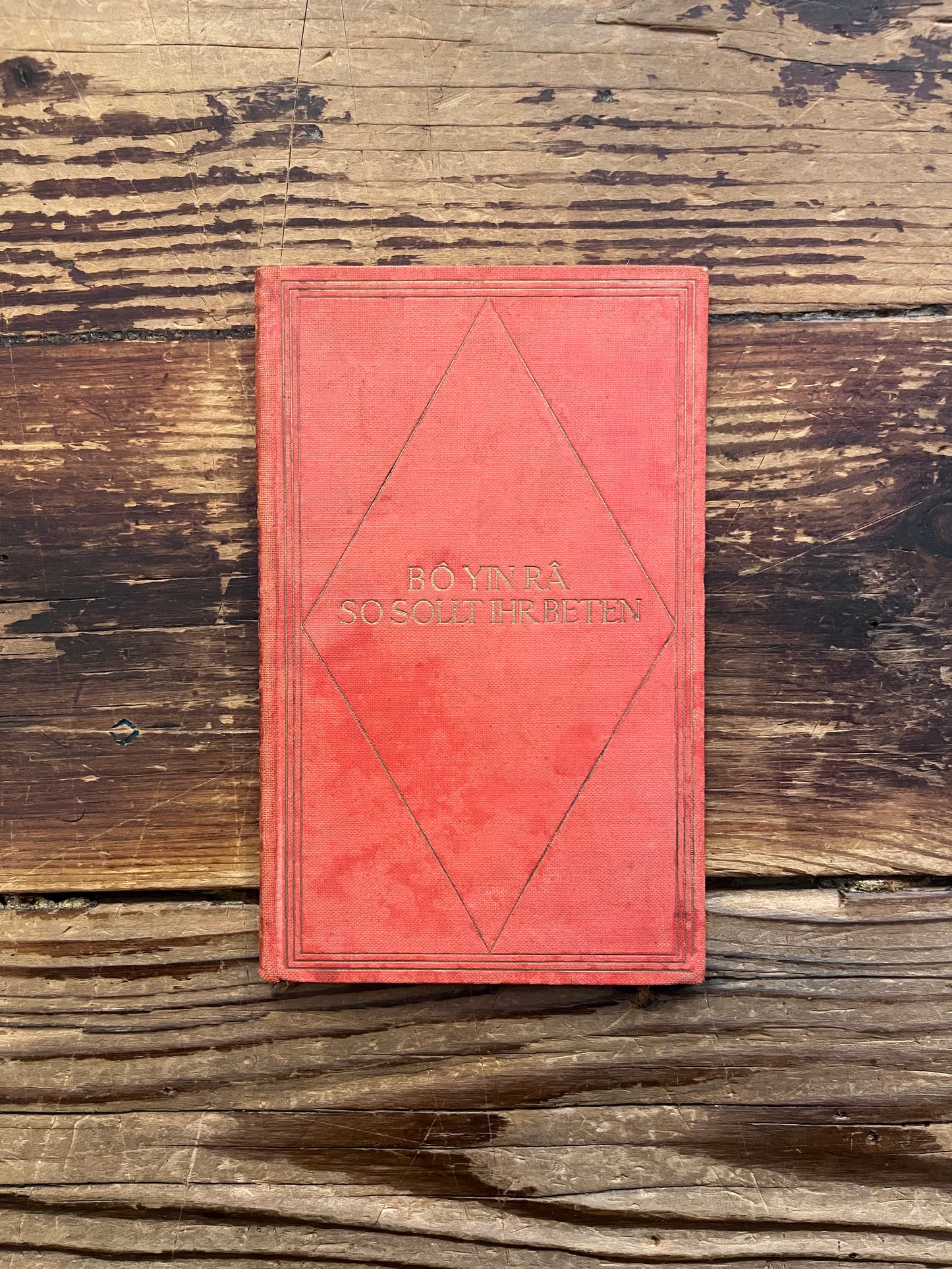 red cloth bound booklet with gold gilded letters with the title 'So Sollt Ihr Beten' by Bo Yin Ra on a wooden surface 
