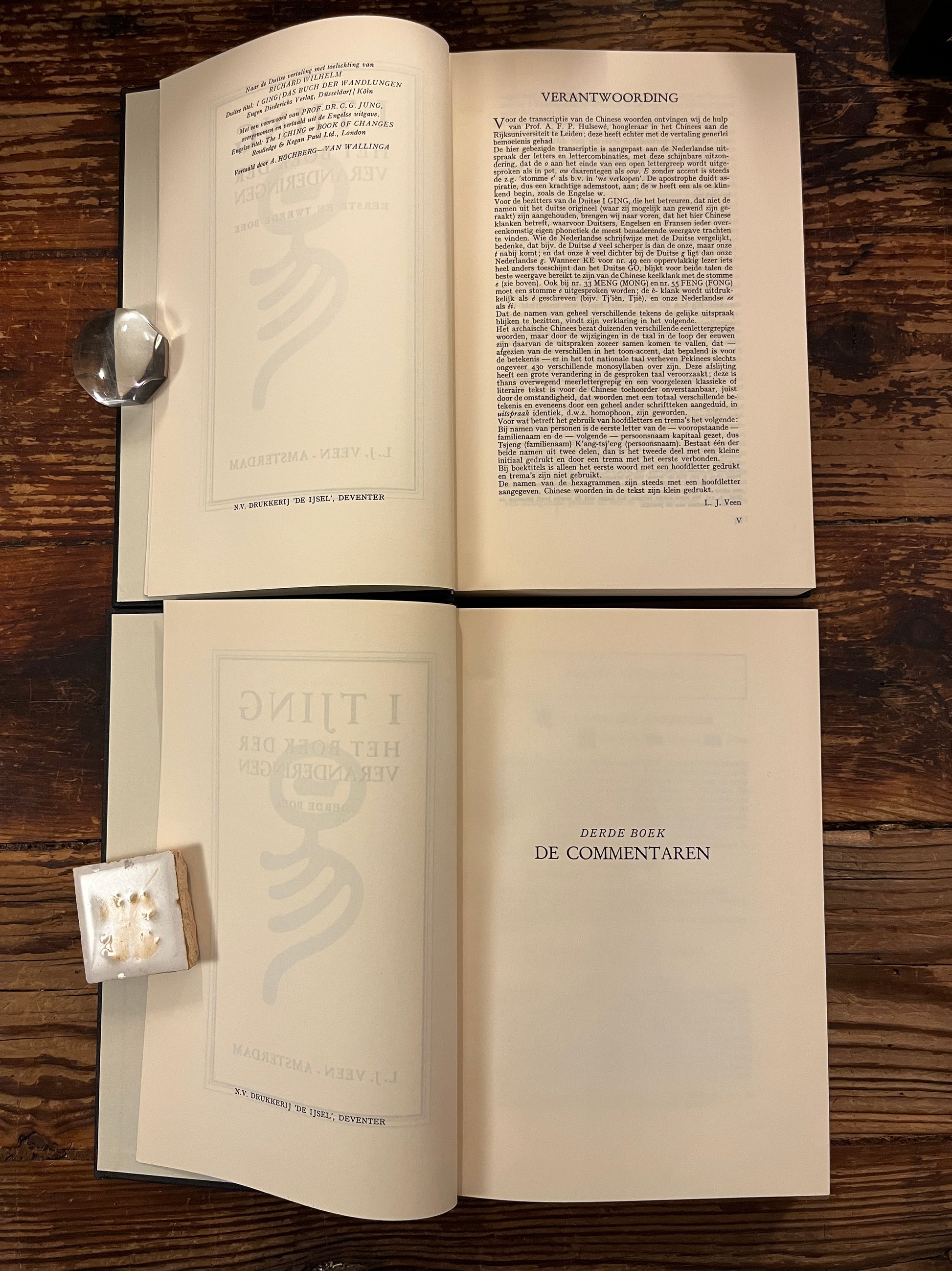 Twee open boeken met de titel 'I Tjing: Het Boek Der Veranderingen' op een houten achtergrond