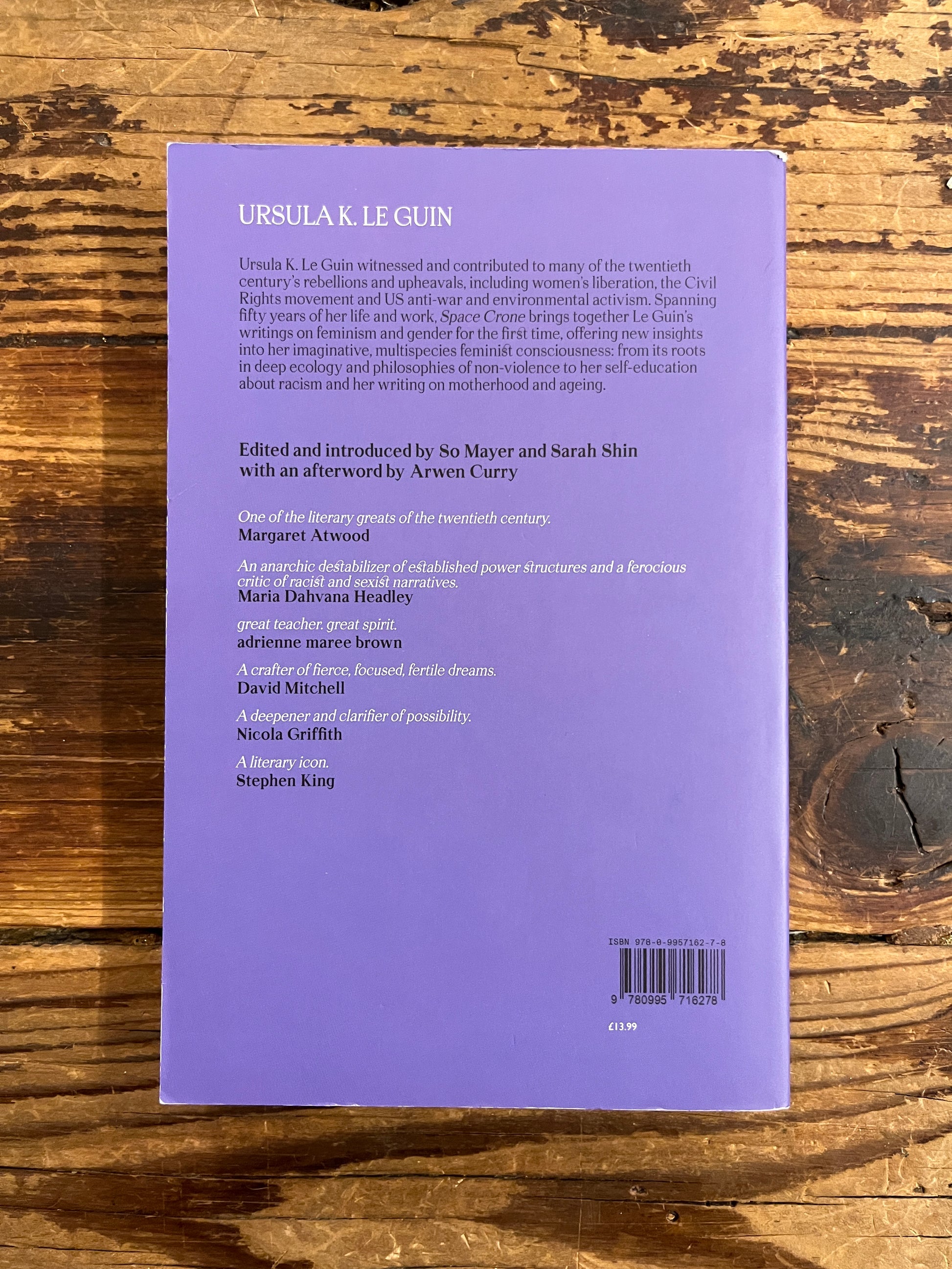 Back cover of book titled 'Space Crone' by Ursula K. Le Guin on a wooden surface