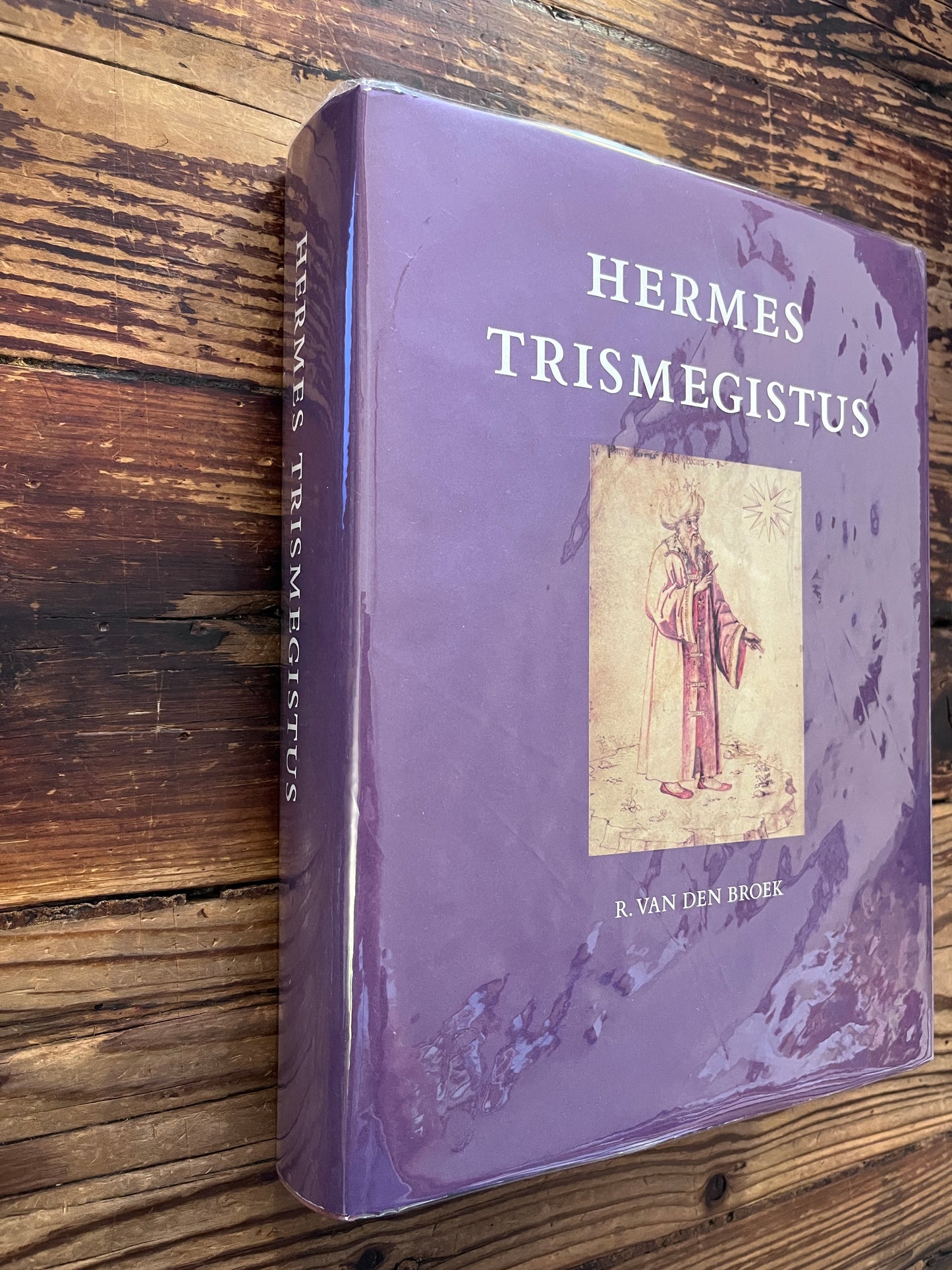 Voorkant  en rug van boek met de titel 'Hermes Trismegistus' door Van den Broek op een houten achtergrond 