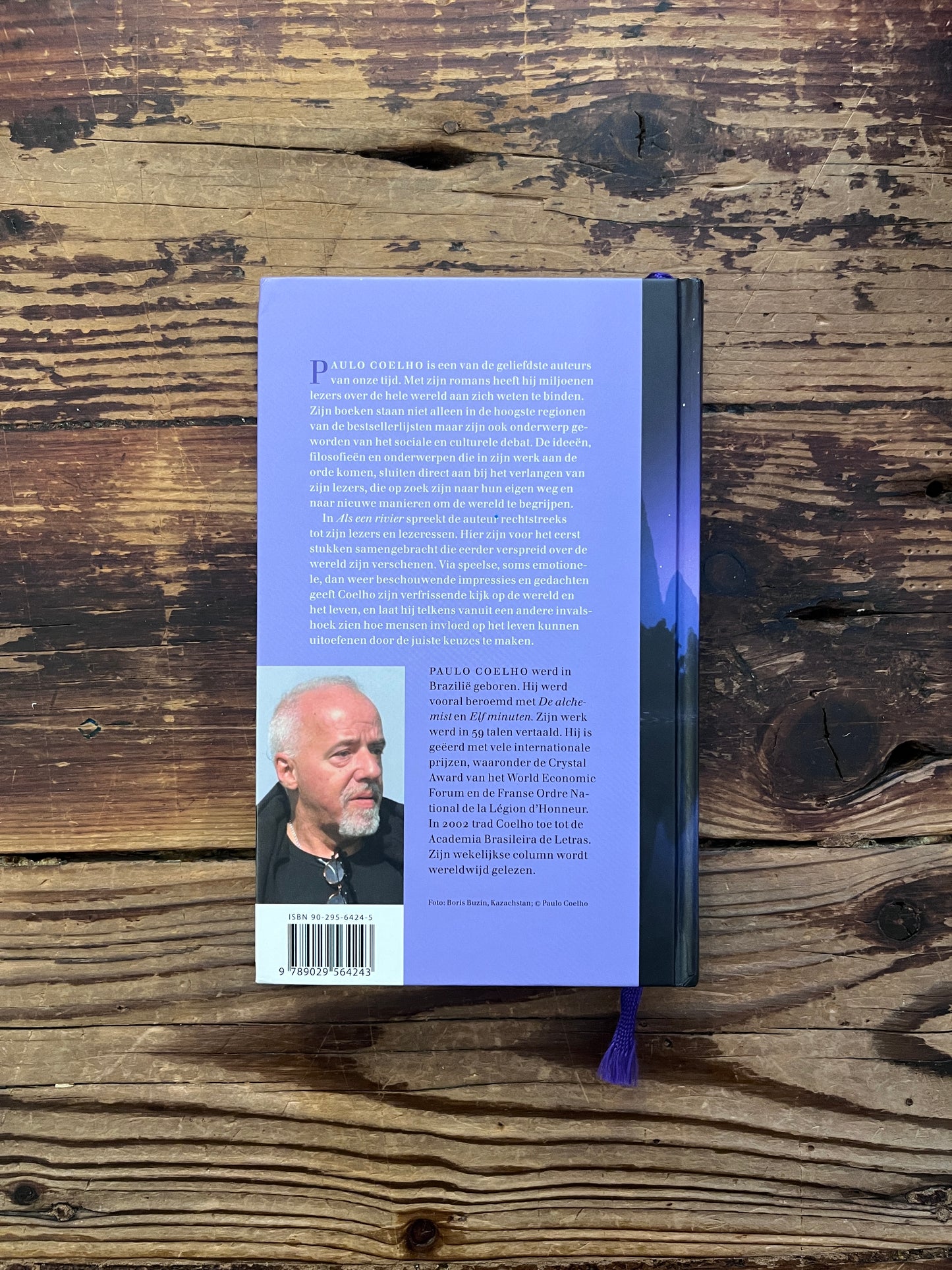 Voorkant van boek met de titel 'Als een rivier' door Paulo Coelho op een houten achtergrond