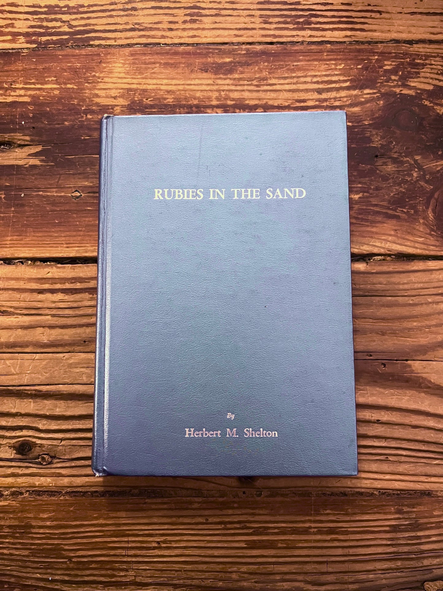 Front cover of book titled 'Rubies in the Sand' by Herbert M. Shelton on a wooden surface