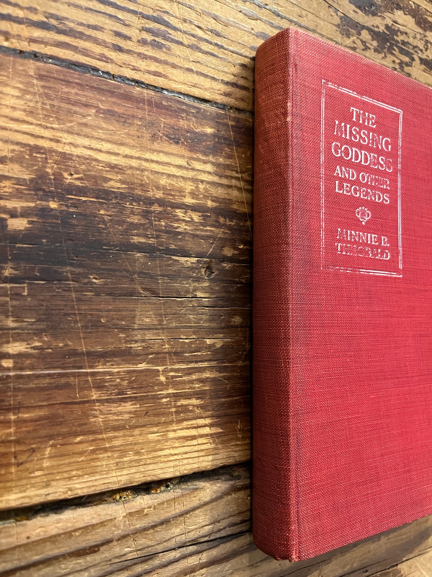 Spine of book titled 'the missing Goddess and other legends' by Minnie Theobald on a wooden surface