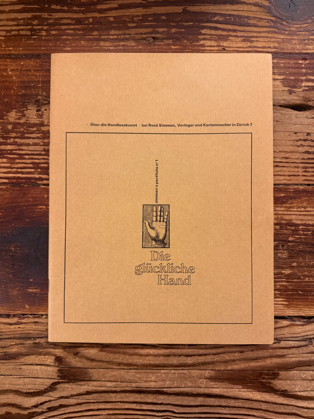Front cover of the paperback 'Simmen's Portfolio No. 1: Die glückliche Hand' on a wooden background 