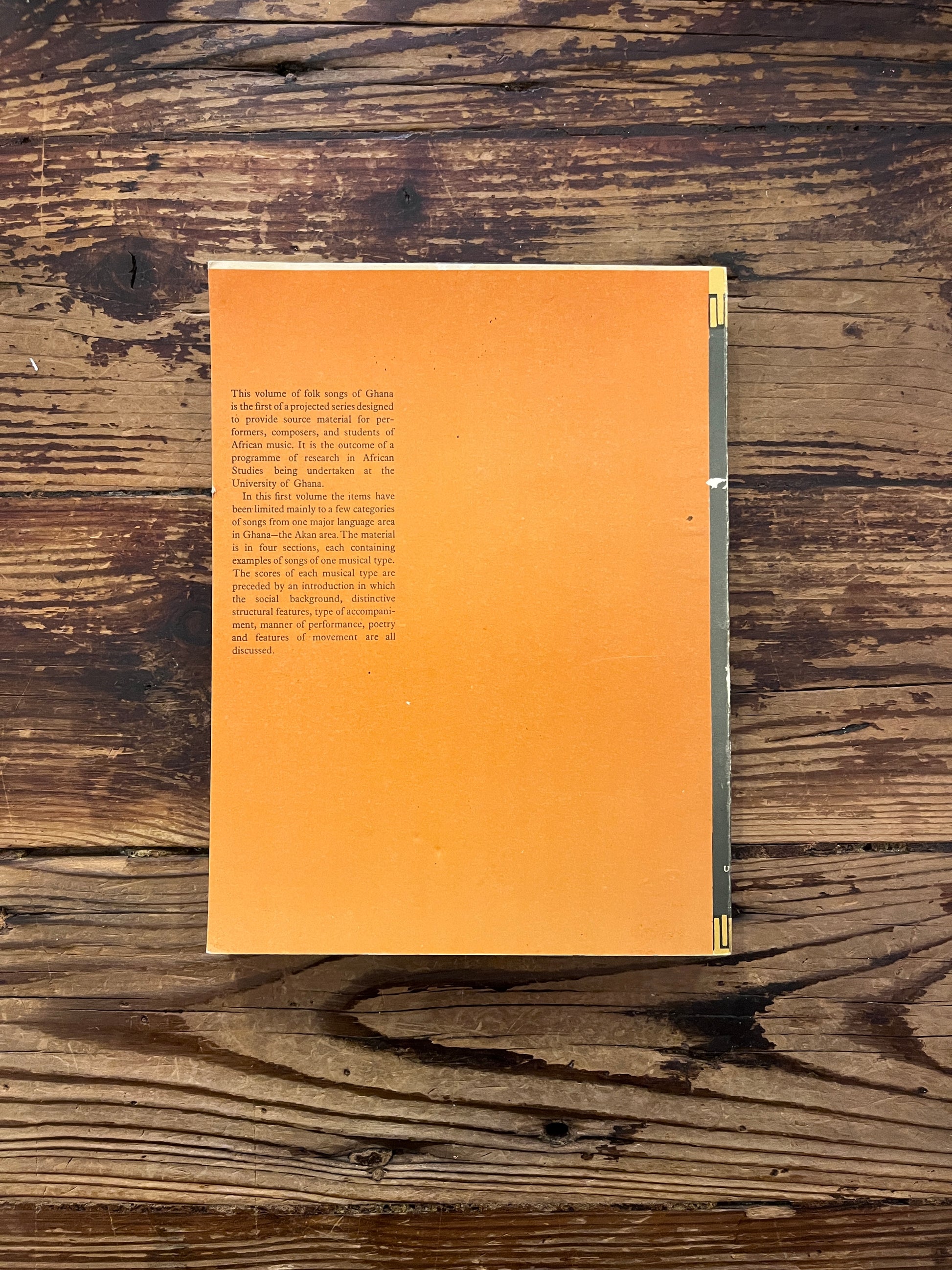 Back cover of book titled 'Folk Songs of Ghana' by J.H. Kwabena Nketia on a wooden surface 