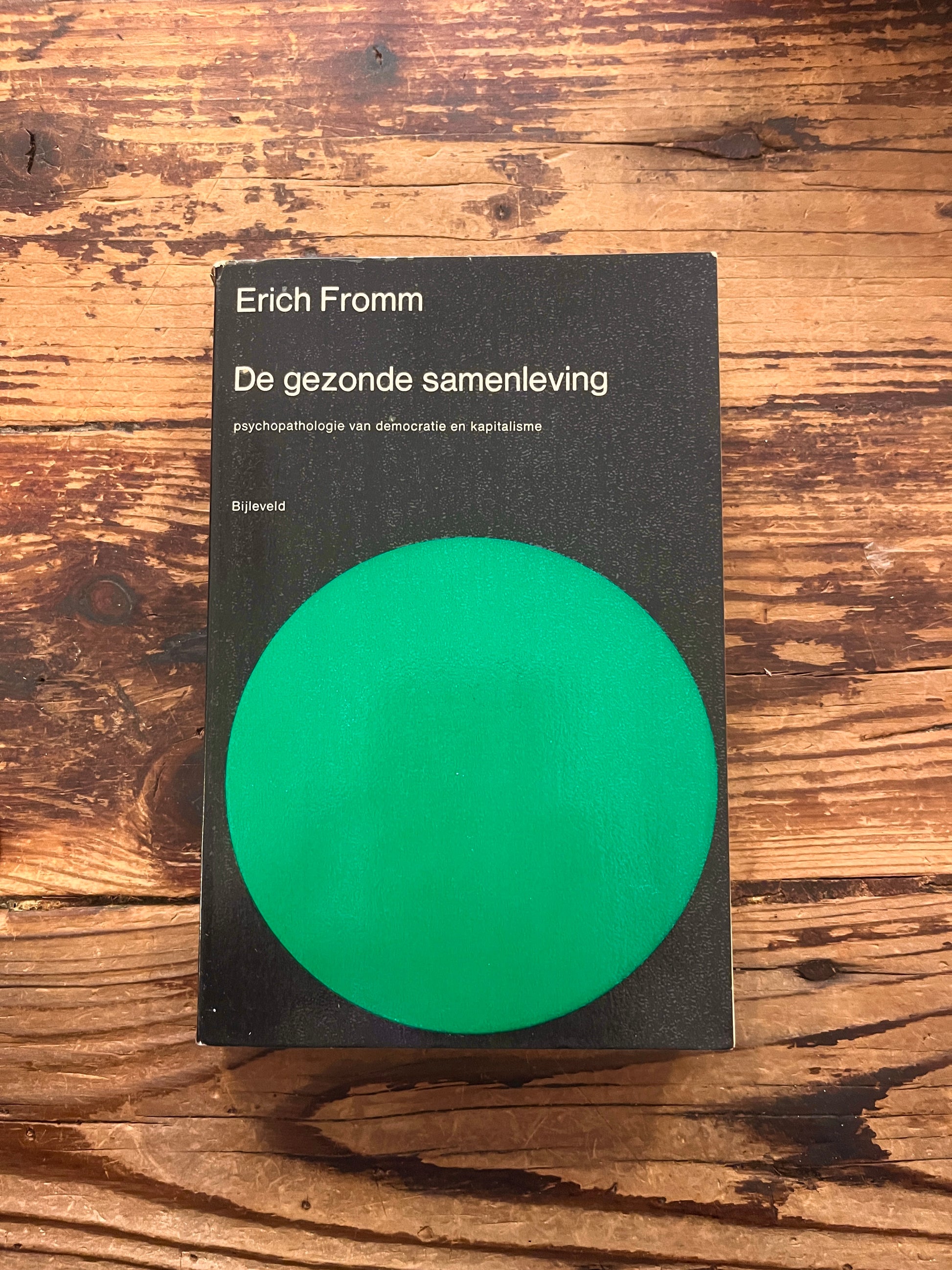 Boek met de titel 'De gezonde samenleving' door Erich Fromm op een houten achtergrond 