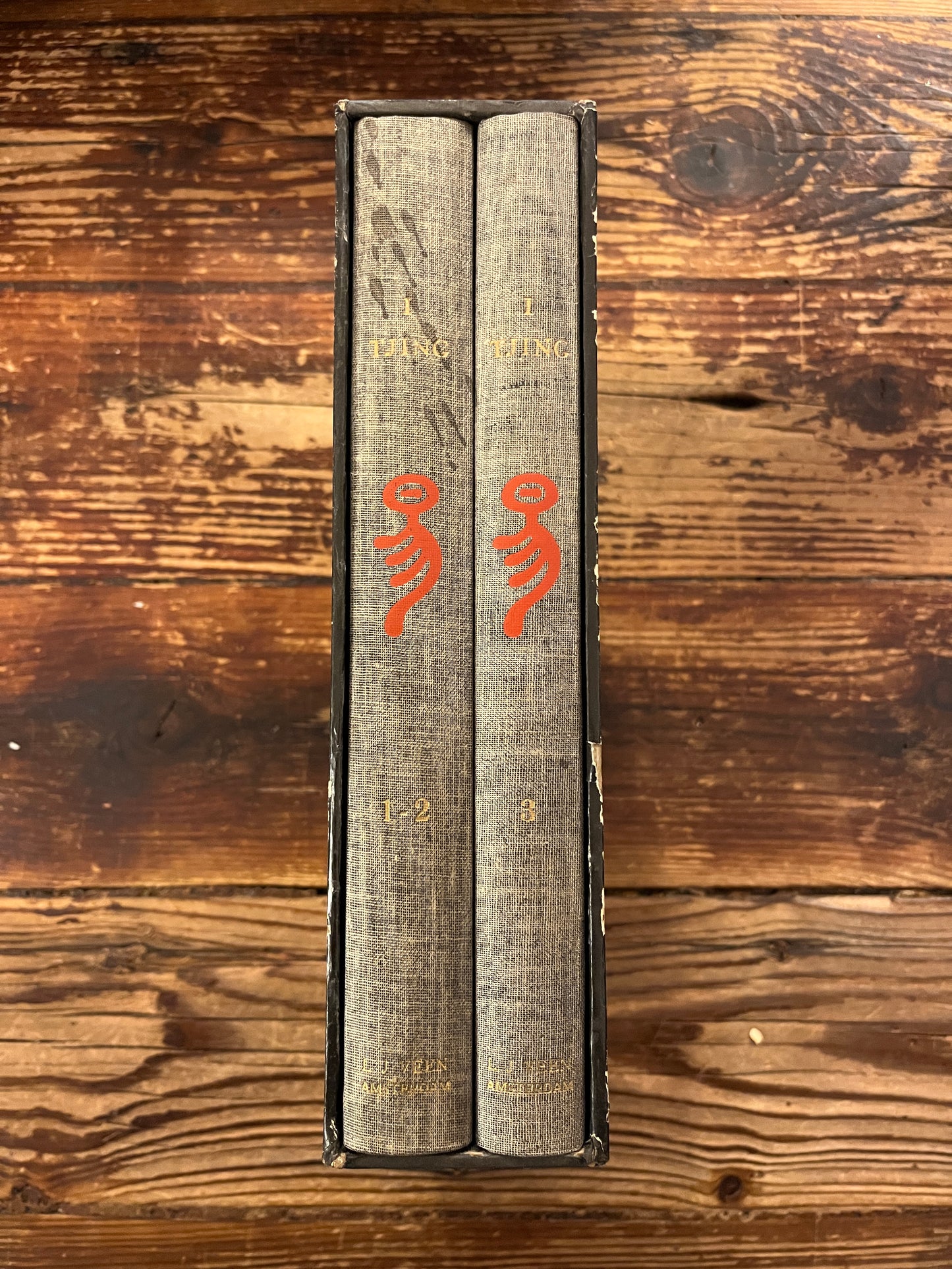 De rug van casette met twee boeken met de titel 'I Tjing: Het Boek Der Veranderingen' op een houten achtergrond