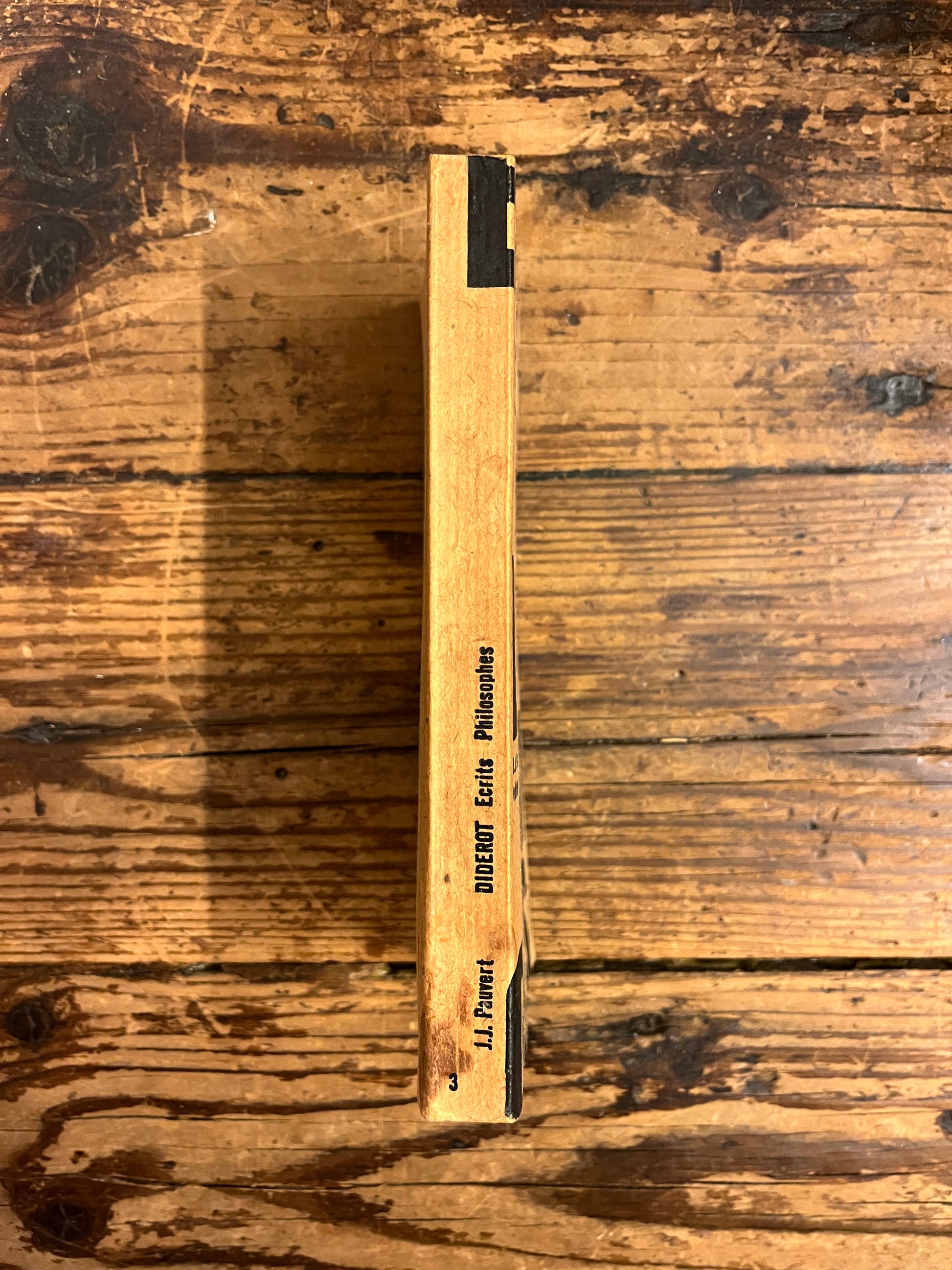 dos du livre "Ecrits philosophiques" par Denis Diderot sur fond de bois. 
Une legere tache est visible au bas du dos du livre.