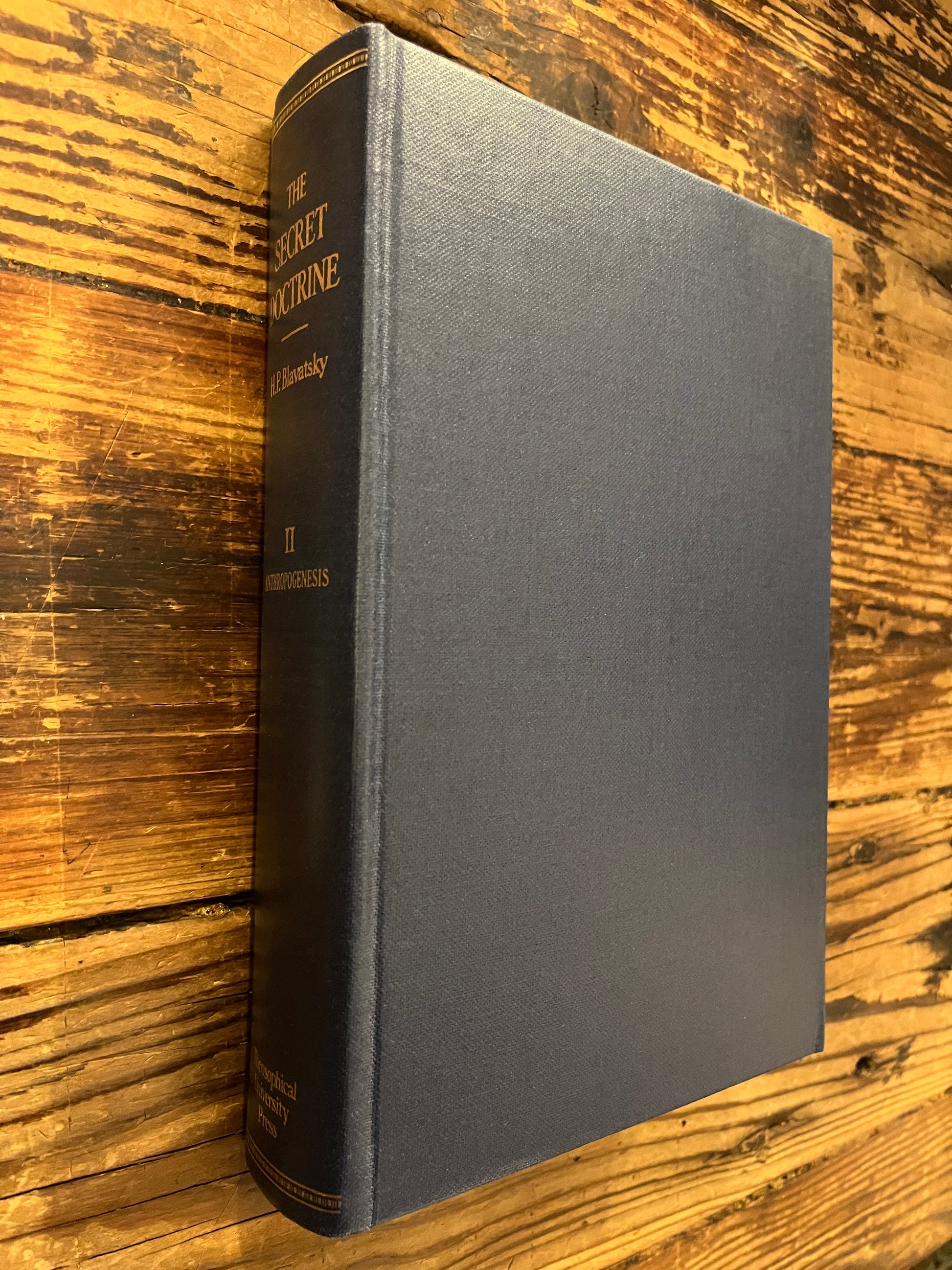 Book without dust jacket titled 'The Secret Doctrine' by H.P. Blavatsky on a wooden surface.