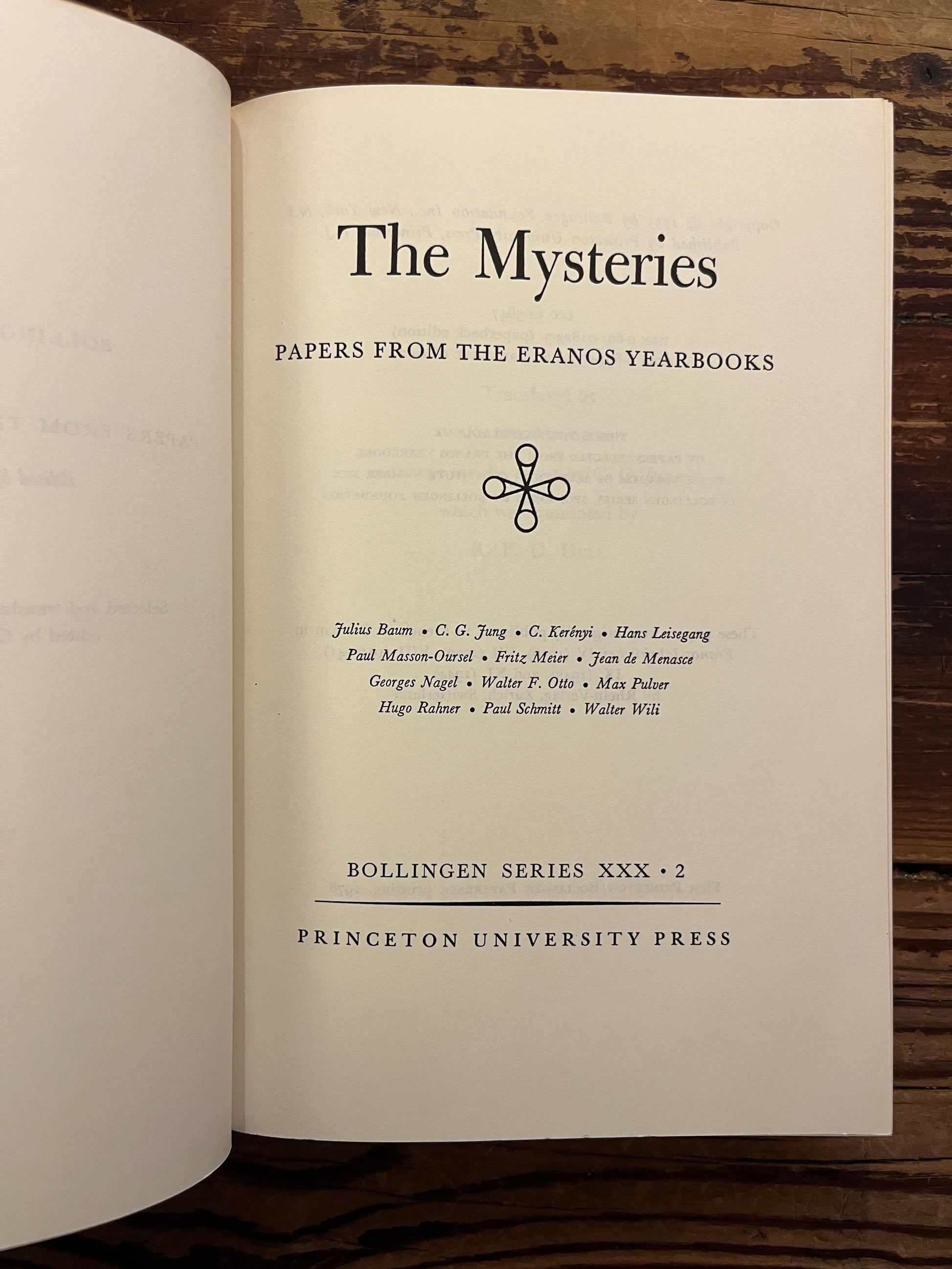 Open book titled 'The Mysteries, papers from the Eranos Yearbooks' on a wooden surface