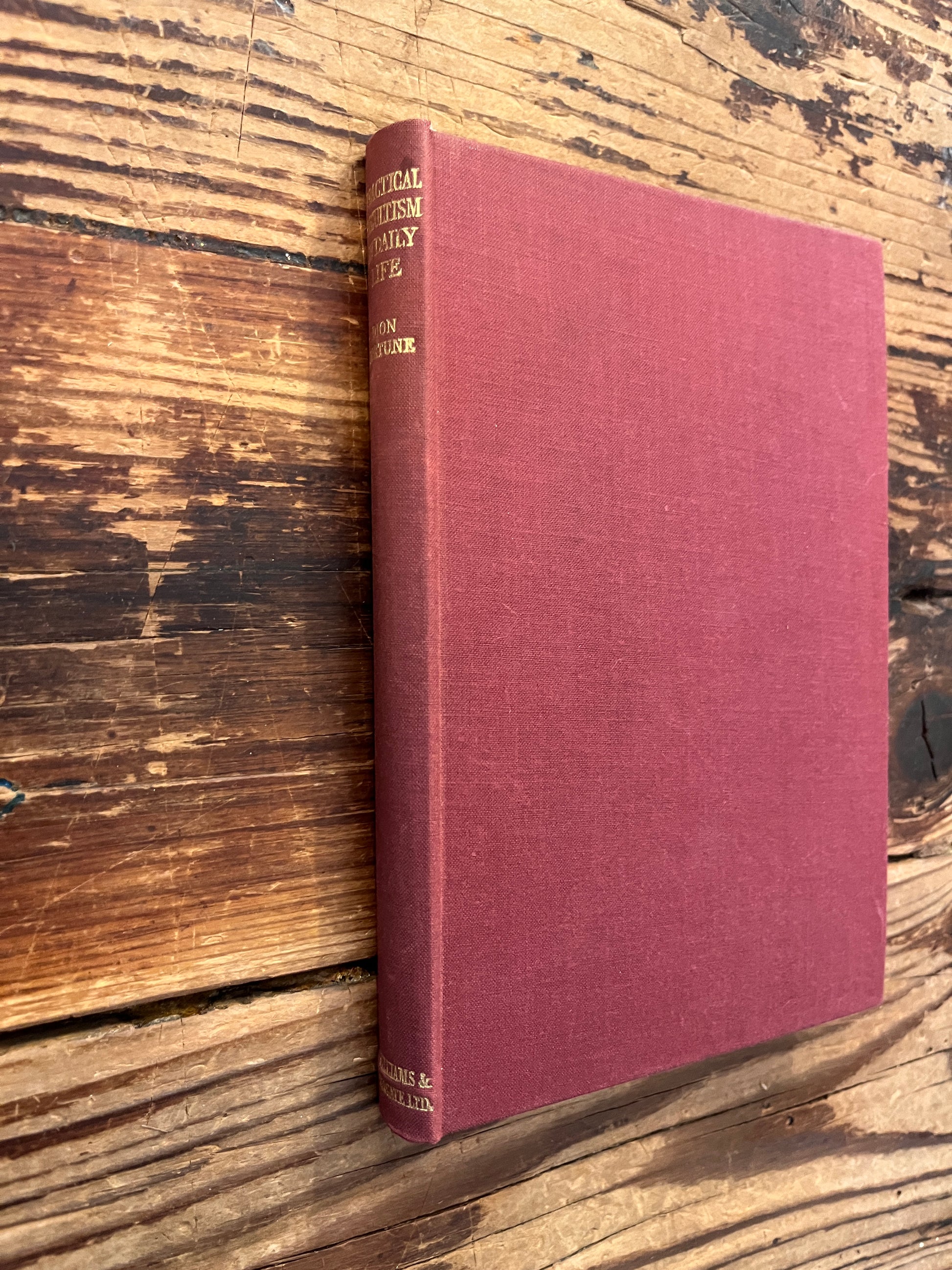 Front cloth cover and spine with gold gilded letters of a rare book with the title 'practical occultism' by Dion Fortune on a wooden surface