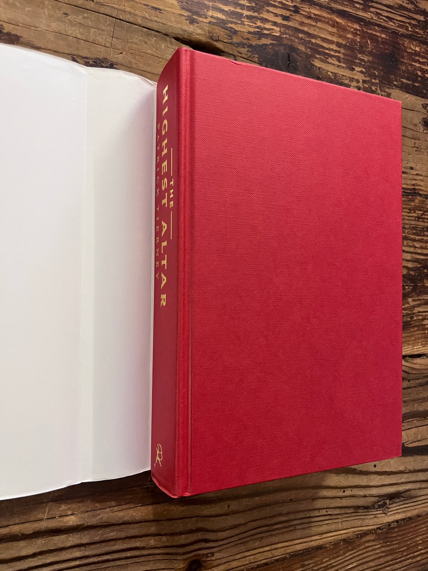 Front cover and spine with out dust-jacket of a book with the title 'The Highest Altar: The Story of Human Sacrifice' by Patrick Tierney is displayed on a wooden surface