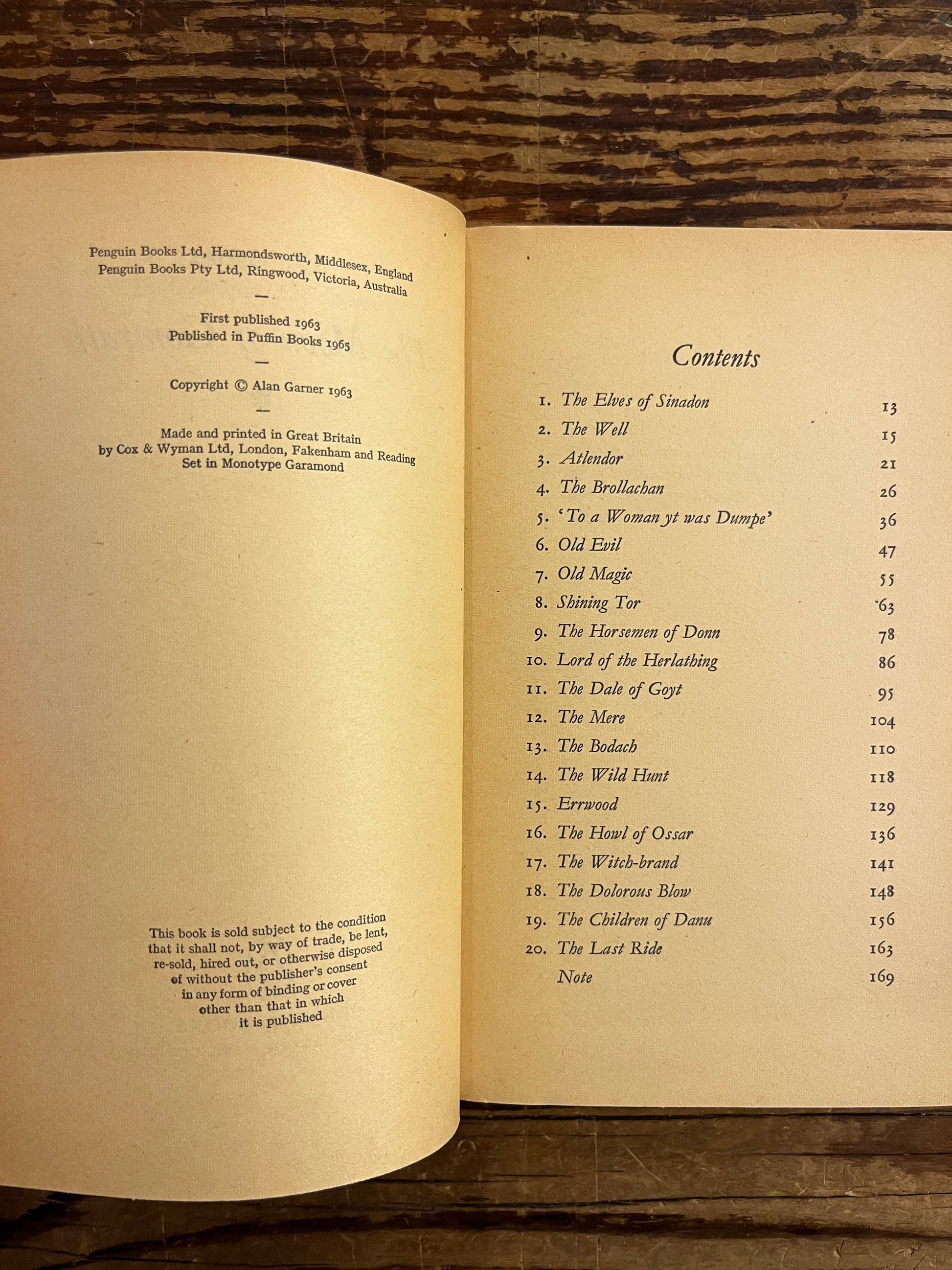 Open book titled of 'The Moon of Gomrath' by Alan Garner on a wooden surface showing the content and publisher page