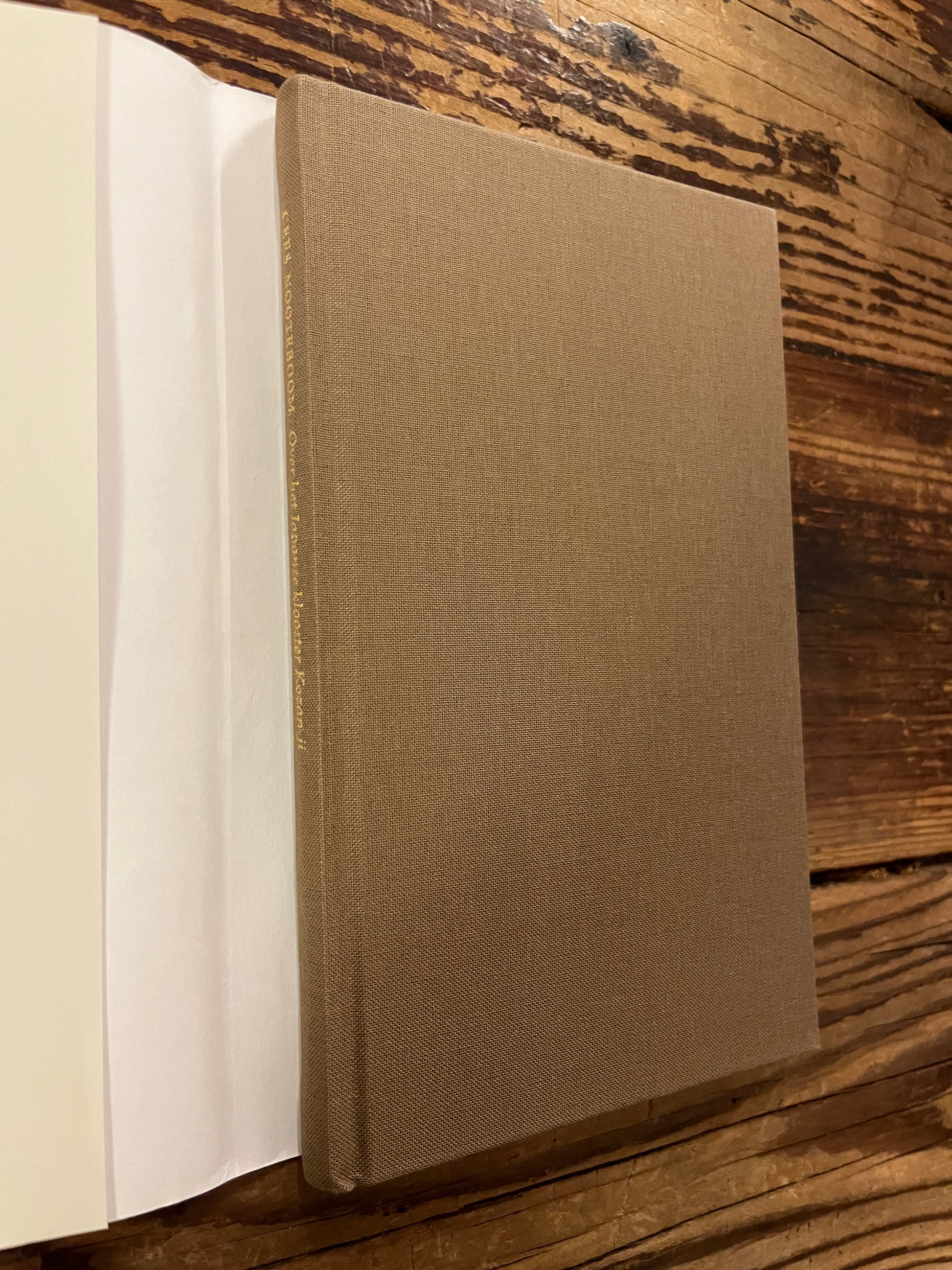 Boek  zonder stof omslag met de titel 'Over het Japanse klooster Kozan-ji en de beroemde dierentekeningen' door Cees Nooteboom, op een houten achtergrond