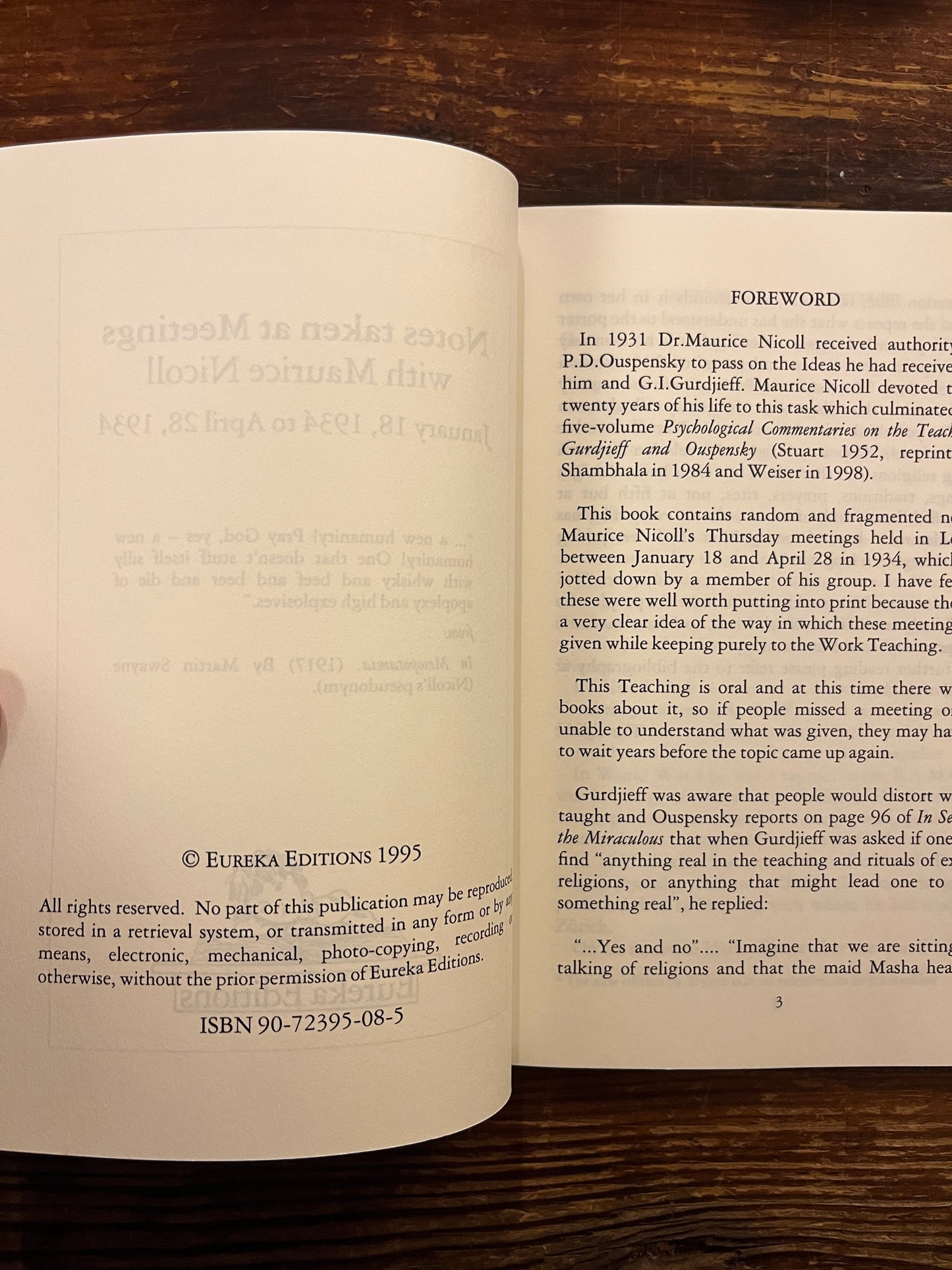 Open book titled'Notes taken at meetings' by Maurice Nicoll on wooden surface 