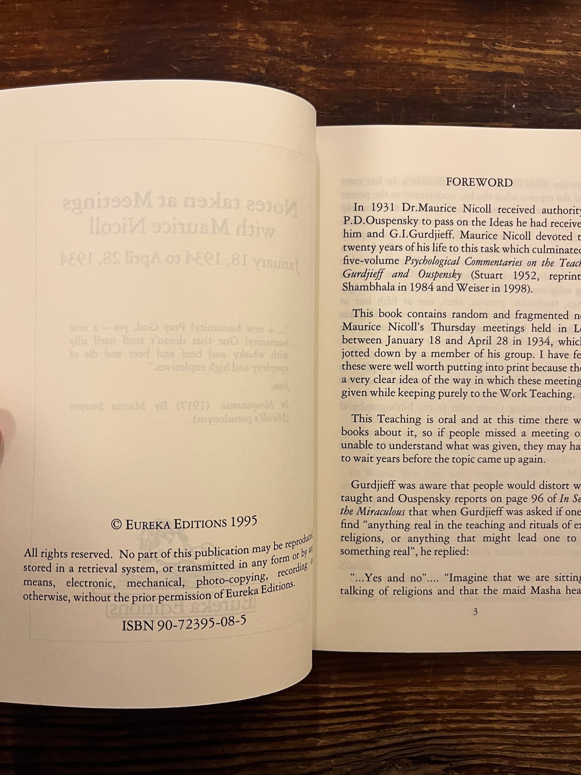 Open book titled'Notes taken at meetings' by Maurice Nicoll on wooden surface 