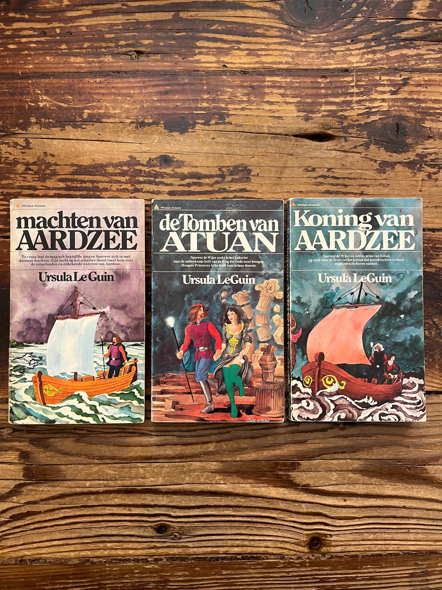Voorkant van de drie delen van de 'Aardzee' trilogie door Ursula K. Le Guin op een houten achtergrond