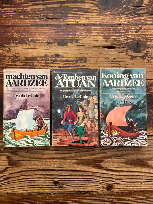 Voorkant van de drie delen van de 'Aardzee' trilogie door Ursula K. Le Guin op een houten achtergrond