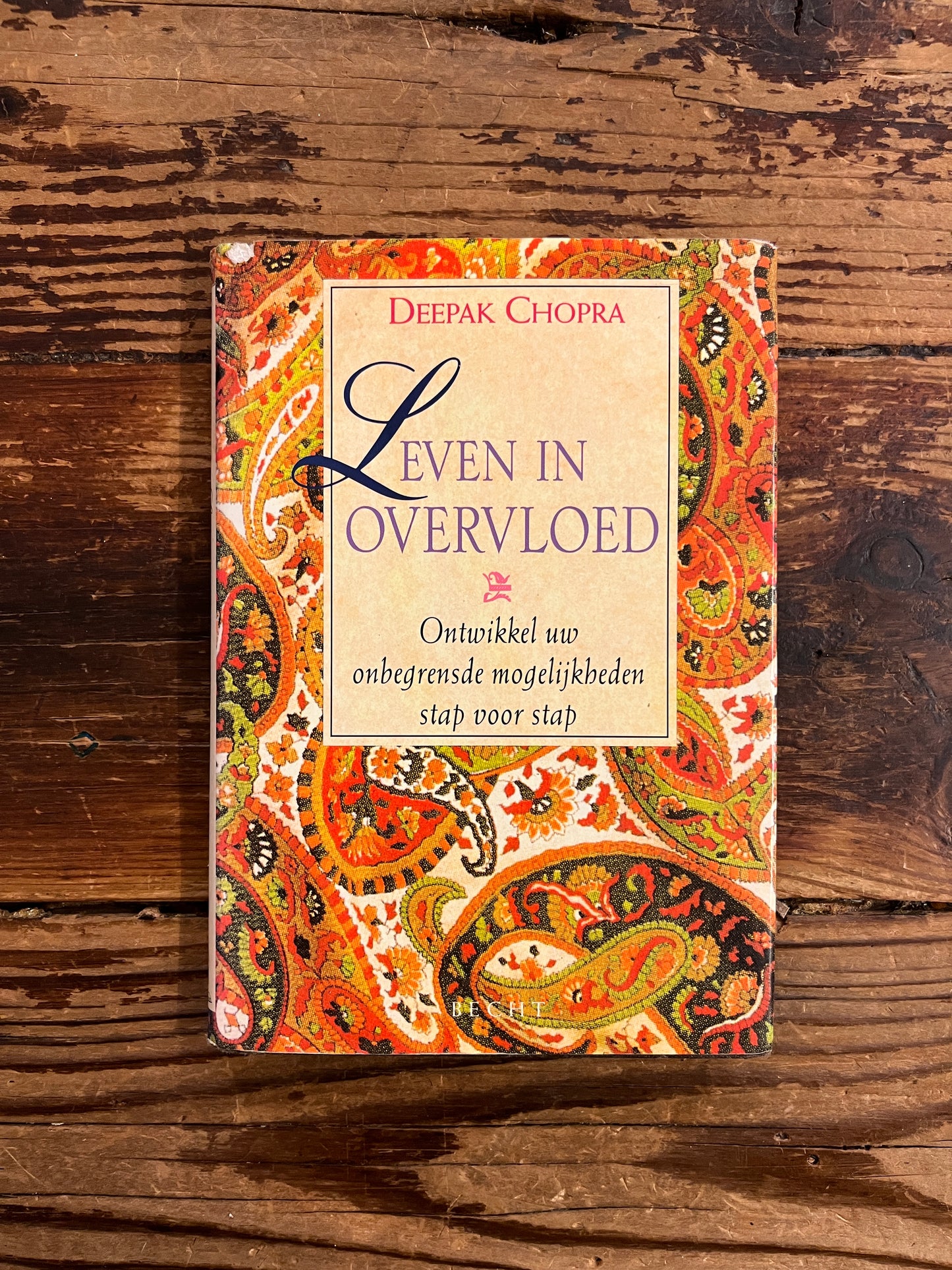 Boek met de titel 'leven in overvloed' door Deepak Chopra op een houten achtergrond
