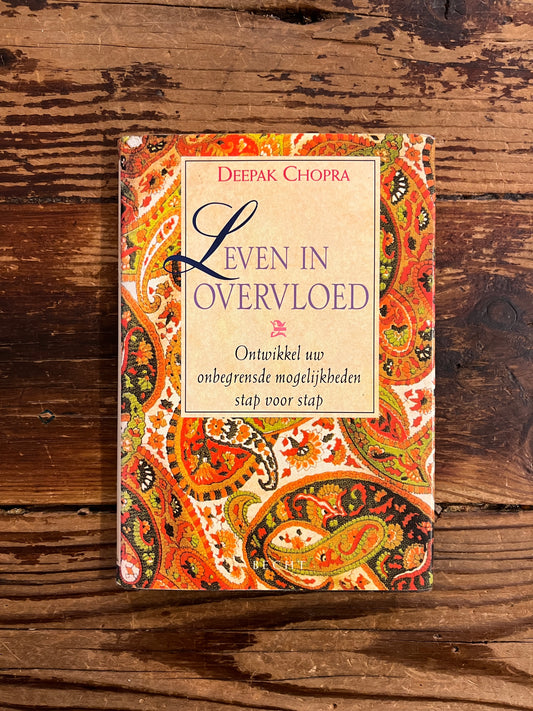 Boek met de titel 'leven in overvloed' door Deepak Chopra op een houten achtergrond