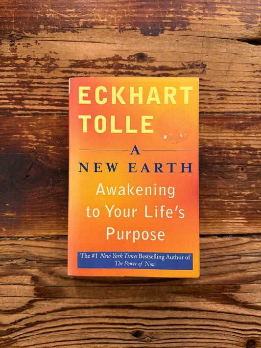 front cover of book titled 'A new Earth' by Eckhart Tolle on a wooden surface 