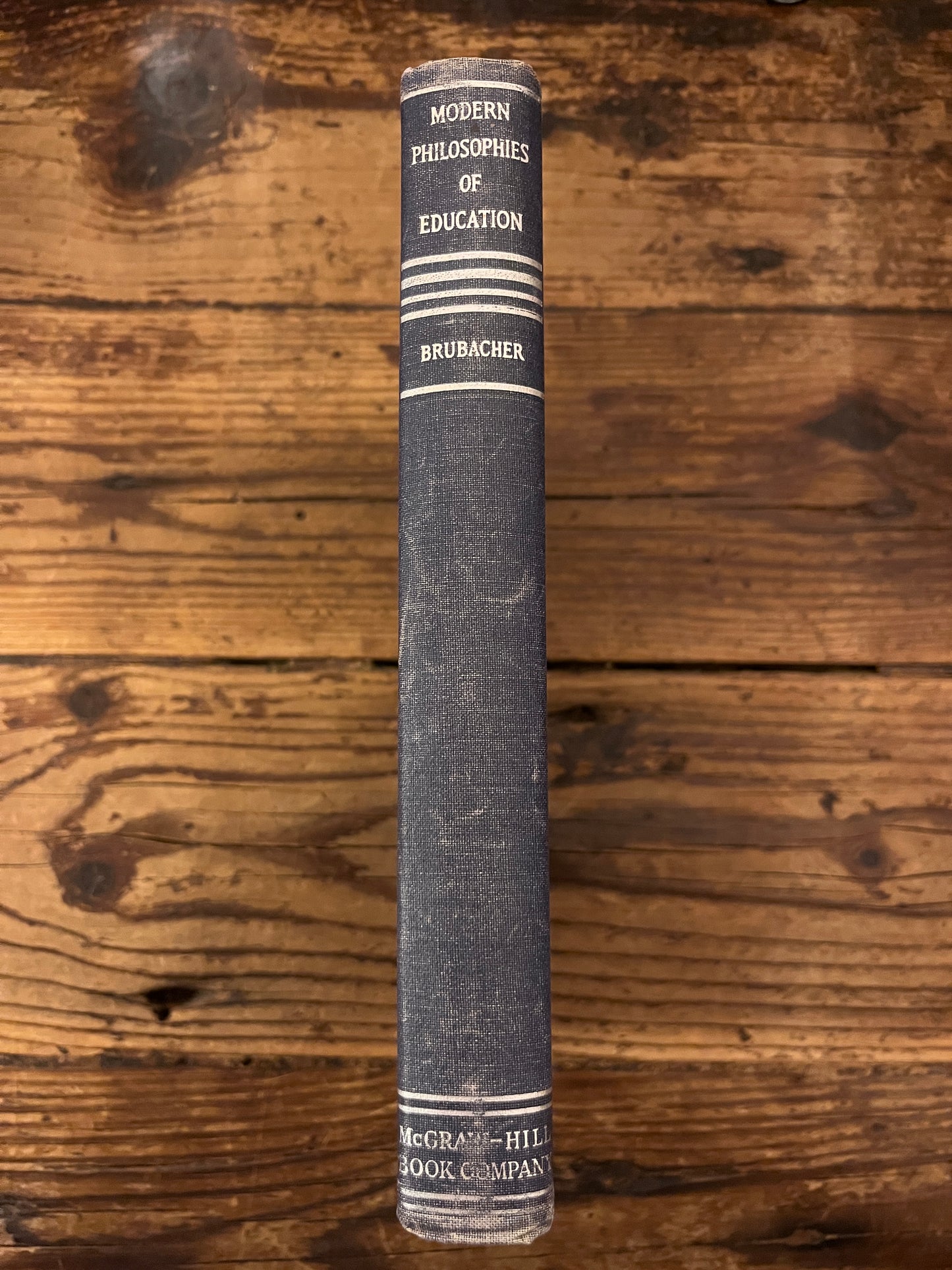 photo of the spine fo the book "modern philosophies of educatio" on a wooden background