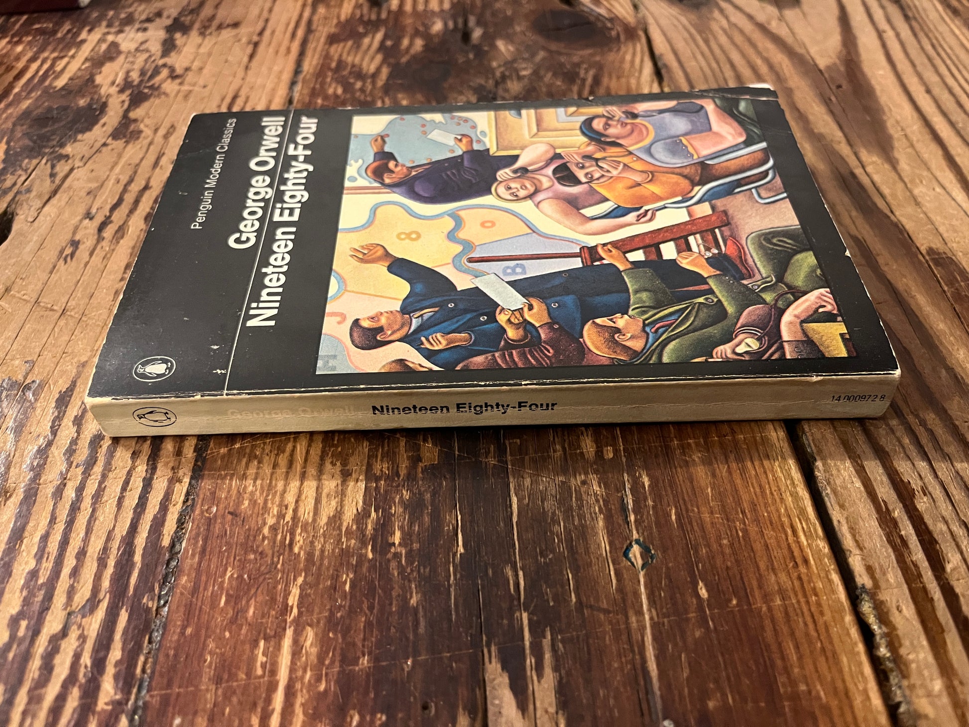 Front cover and spine of  book titled 'Nineteen Eighty-Four' by George Orwell on a wooden surface