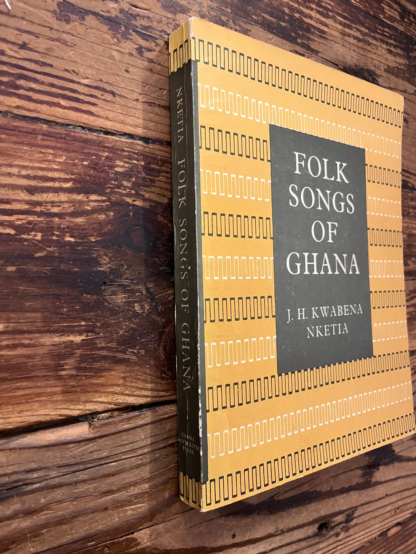 Spine and front cover of book titled 'Folk Songs of Ghana' by J.H. Kwabena Nketia on a wooden surface 