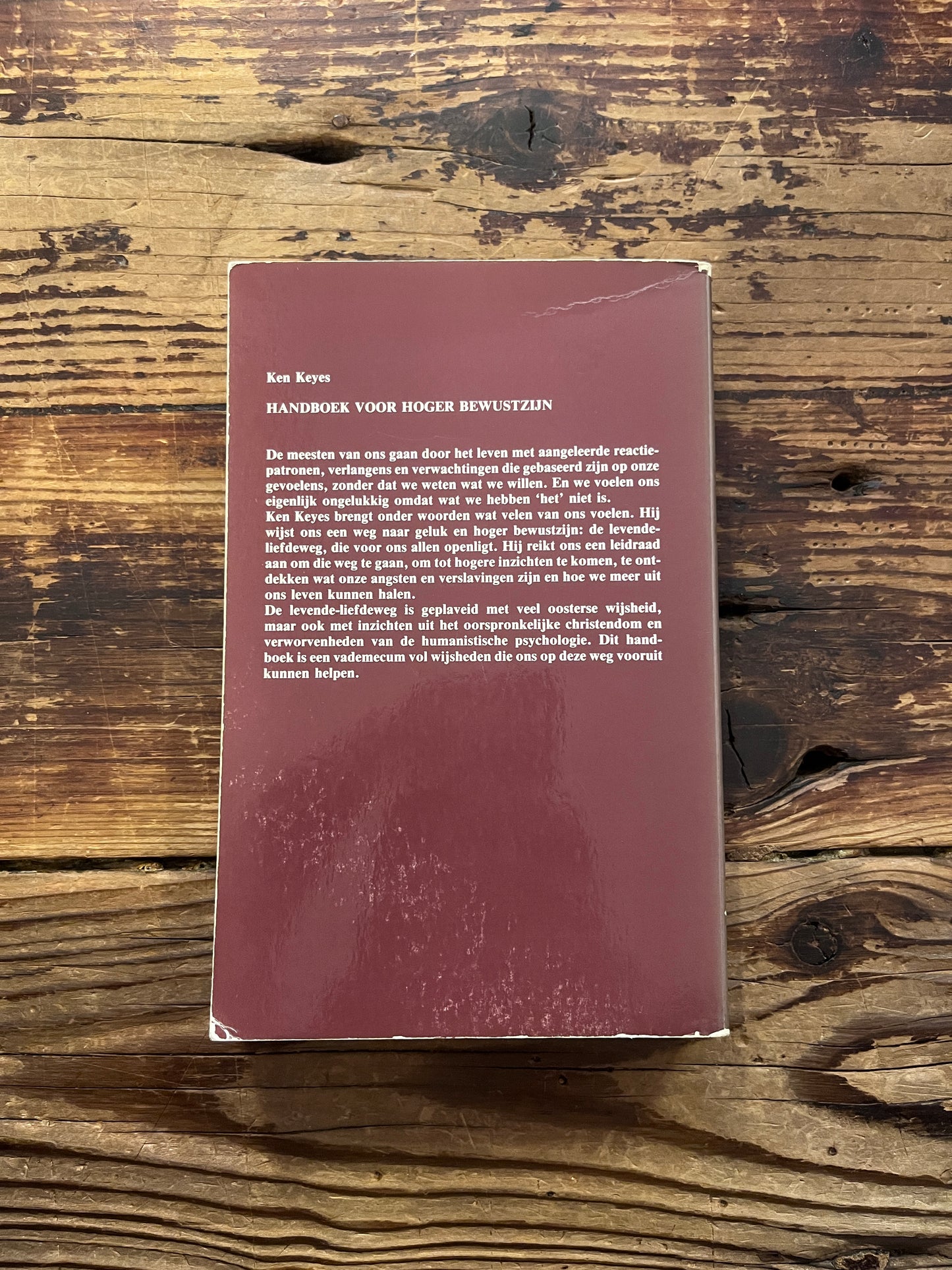 Achterkant van boek 'Handboek voor hoger bewustzijn' door Ken Keyes op een houten achtergrond 