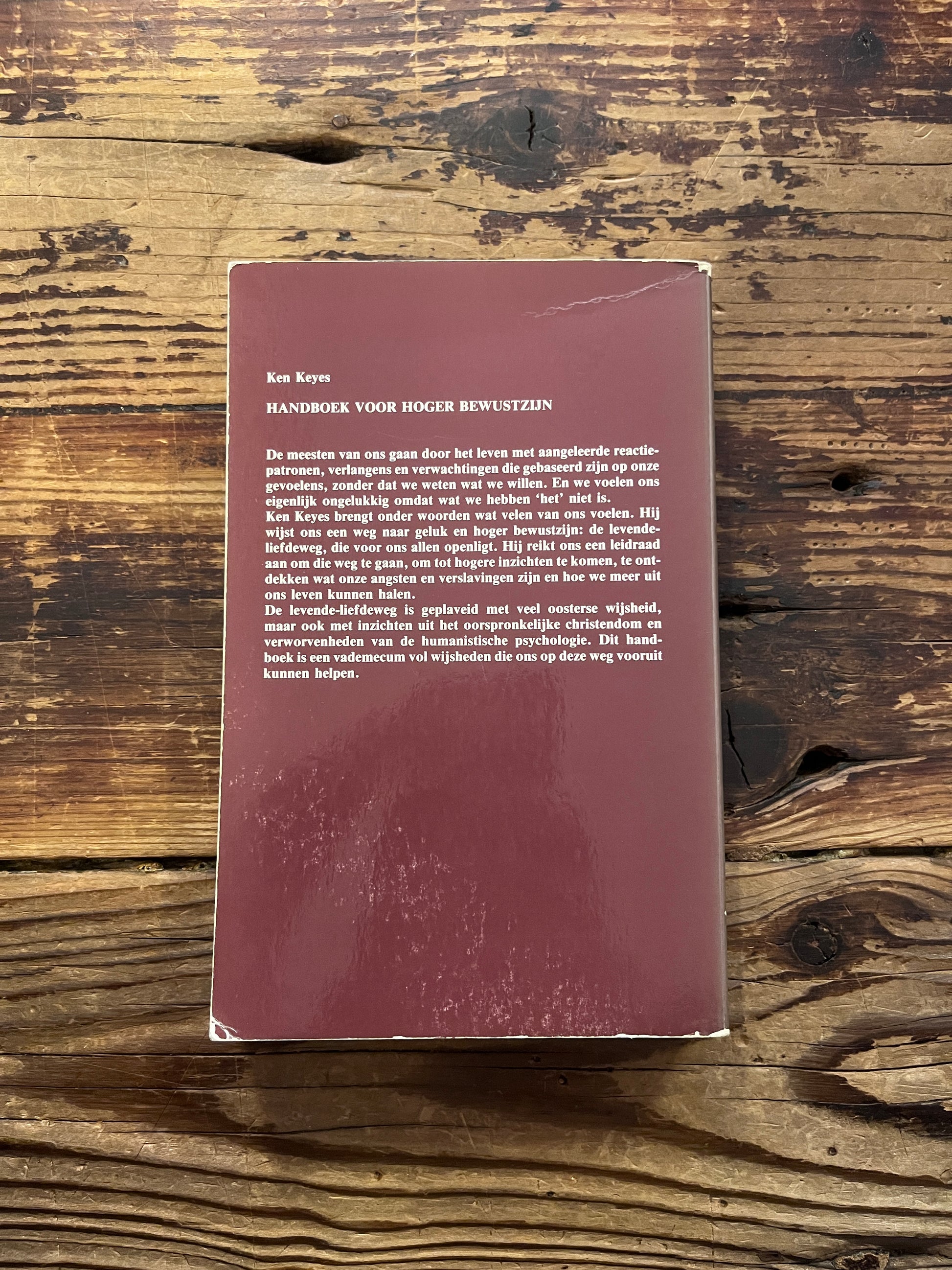 Achterkant van boek 'Handboek voor hoger bewustzijn' door Ken Keyes op een houten achtergrond 