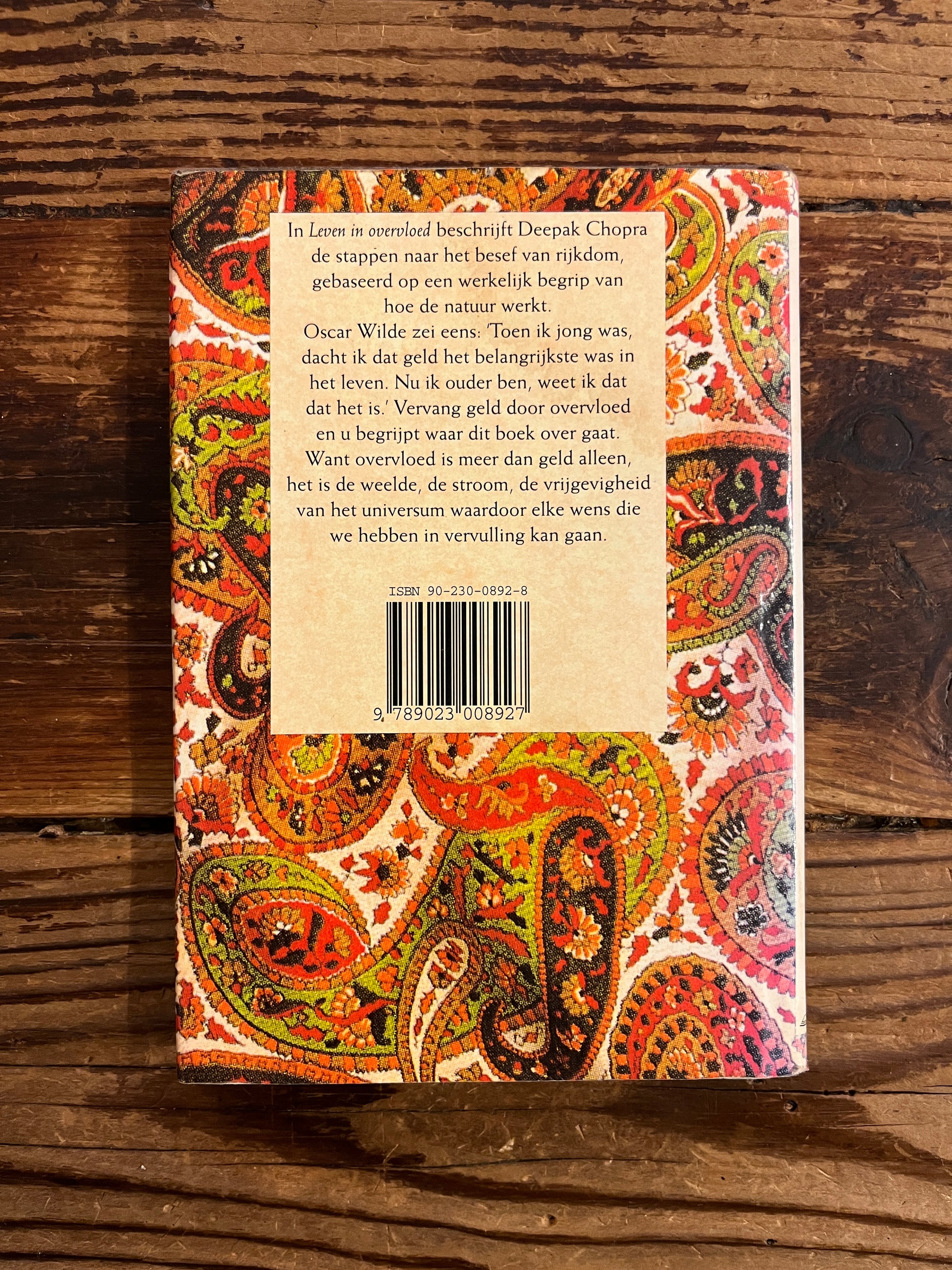 achterkant van Boek met de titel 'leven in overvloed' door Deepak Chopra op een houten achtergrond