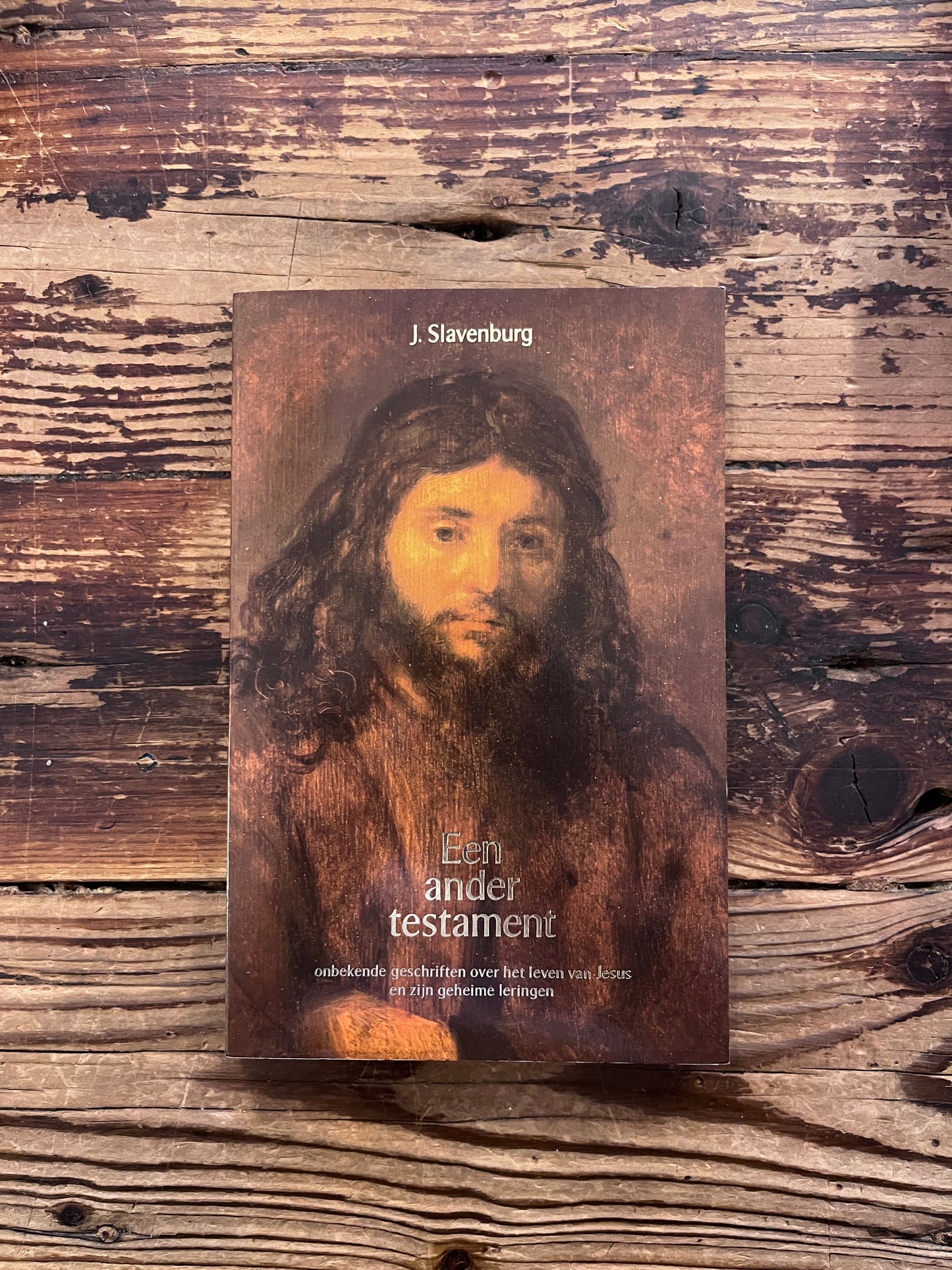 Voorkant van boek met de titel 'Een ander testament' door J. Slavenburg op een houten achtergrond 