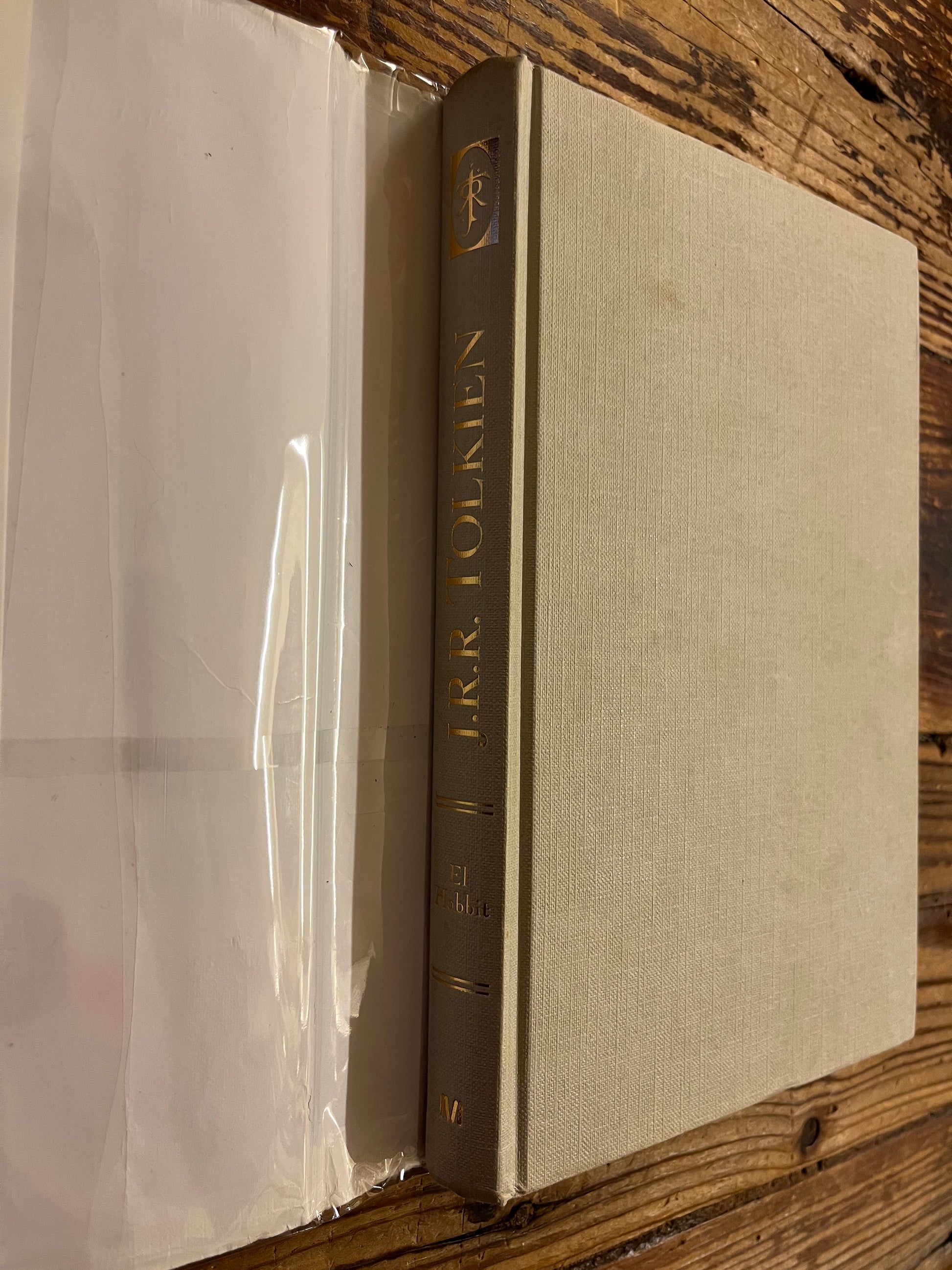  'The Hobbit' by J.R.R. Tolkien on a wooden surface showing the gilded cloth book under the dust jacket 