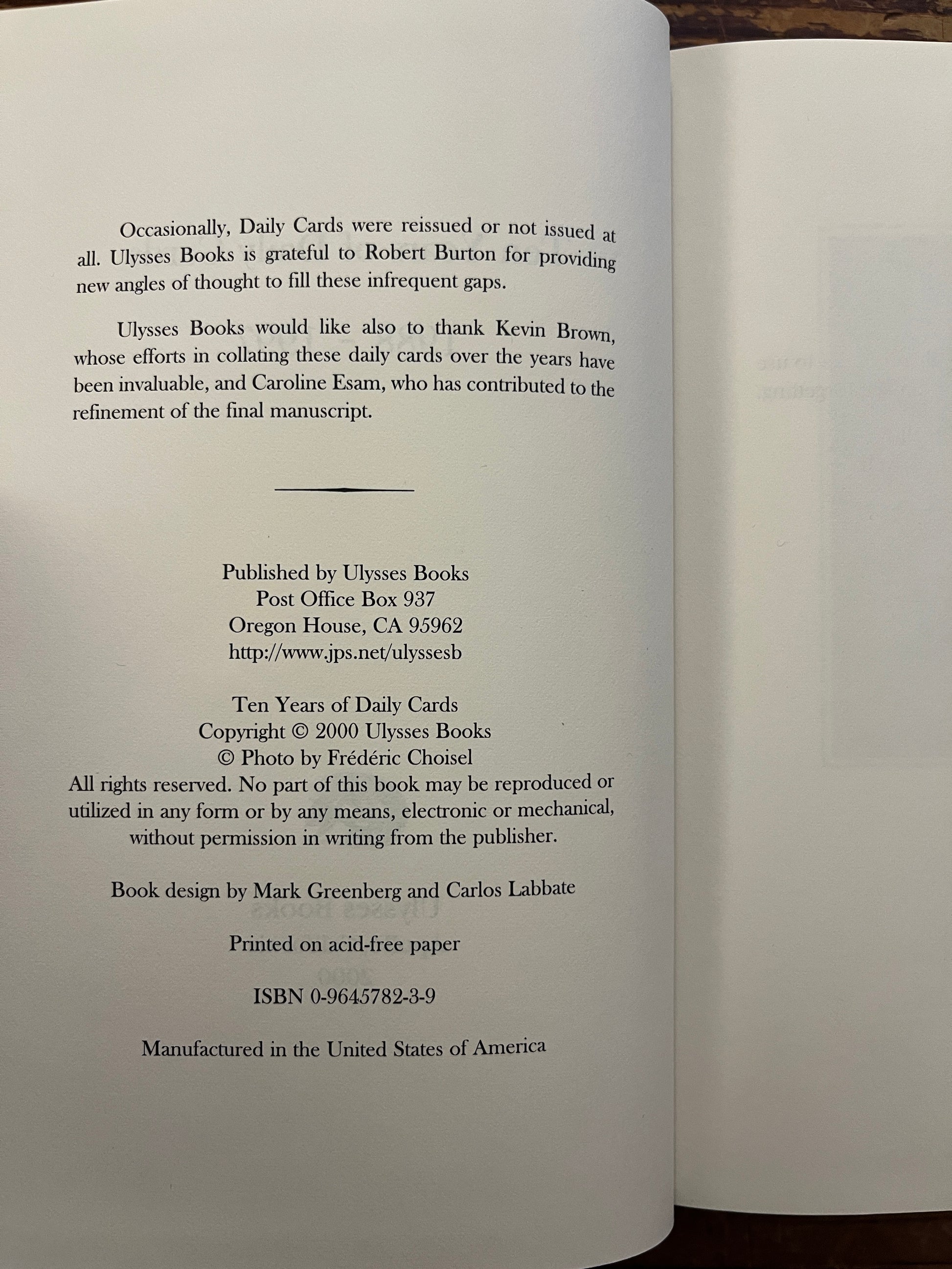 Open book with the title 'Ten Years of Daily Cards' by Robert Burton on a wooden surface