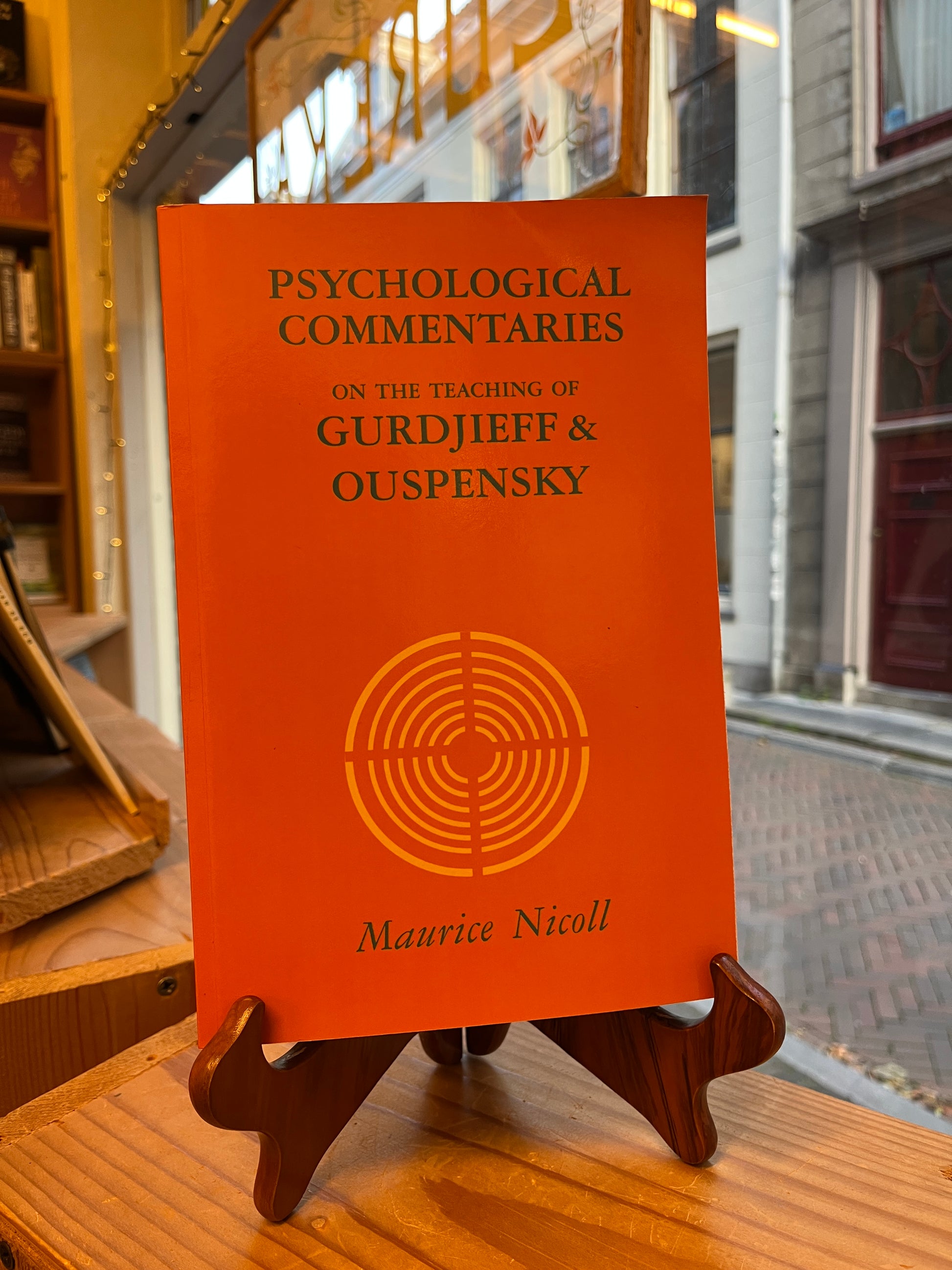 Orange book titled 'Psychological Commentaries on the Teaching of Gurdjieff & Ouspensky' held by a wooden stand.