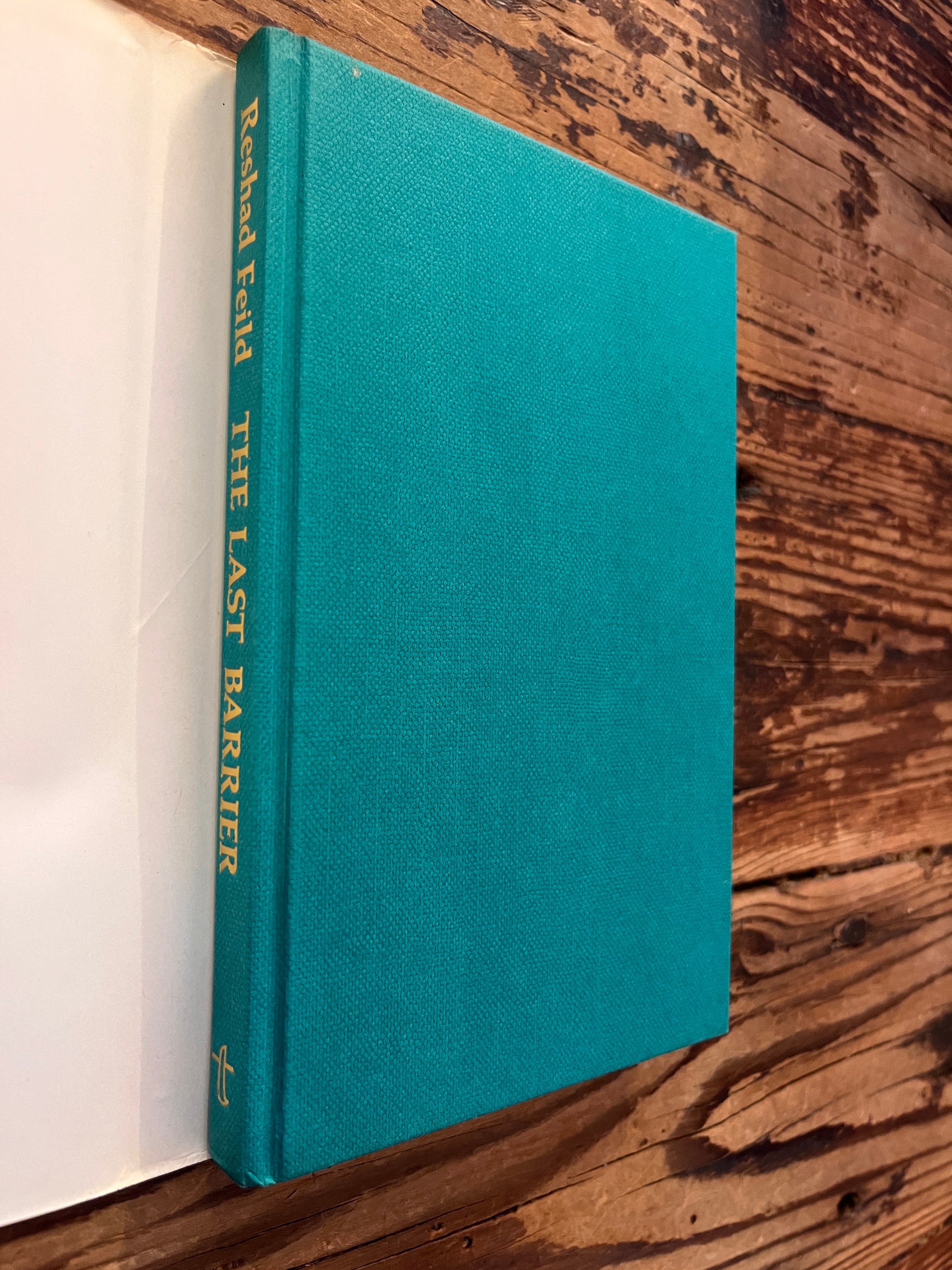 Front cover and spine of book with the title 'the Last Barrier,a sufi journey' by Reshad Feild on a wooden surface 