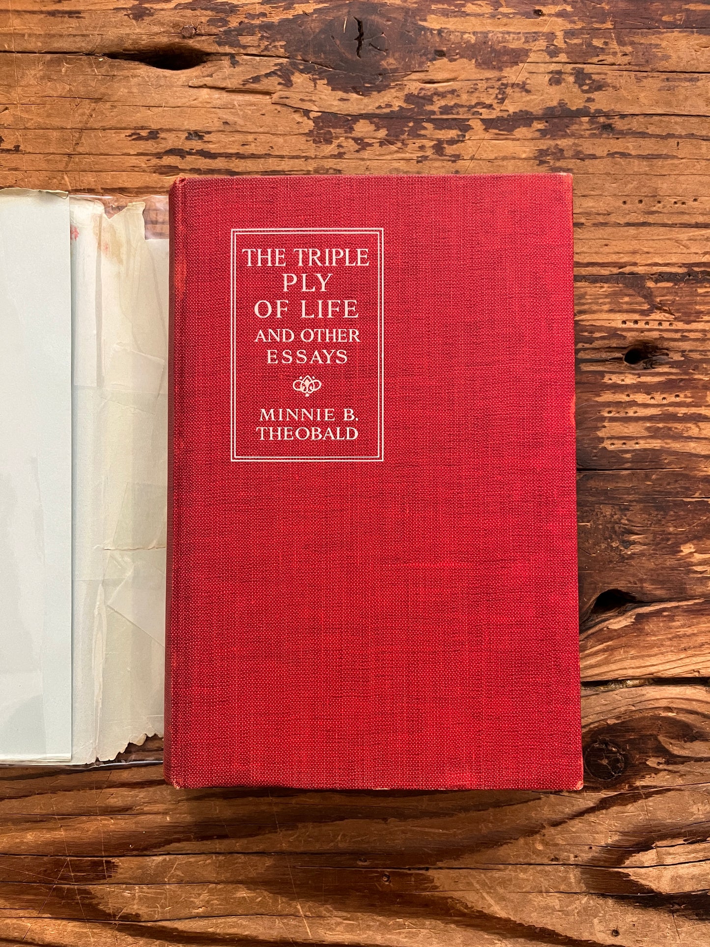 Red cloth cover book titled 'The Triple Ply of Life' by Minnie E. Theobald on a wooden surface