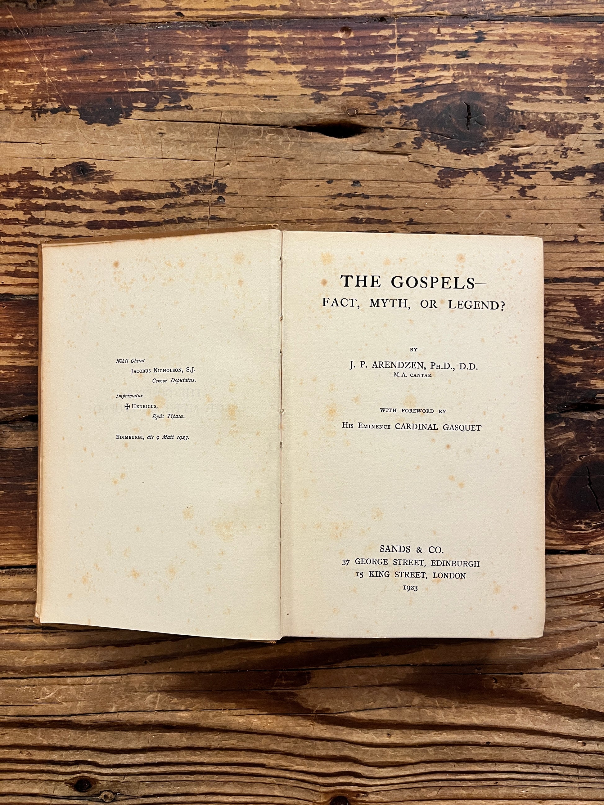 Open book with the title 'the gospels, fact, myth or legend ? by J.P. Arendzen Ph.D. on a wooden surface
