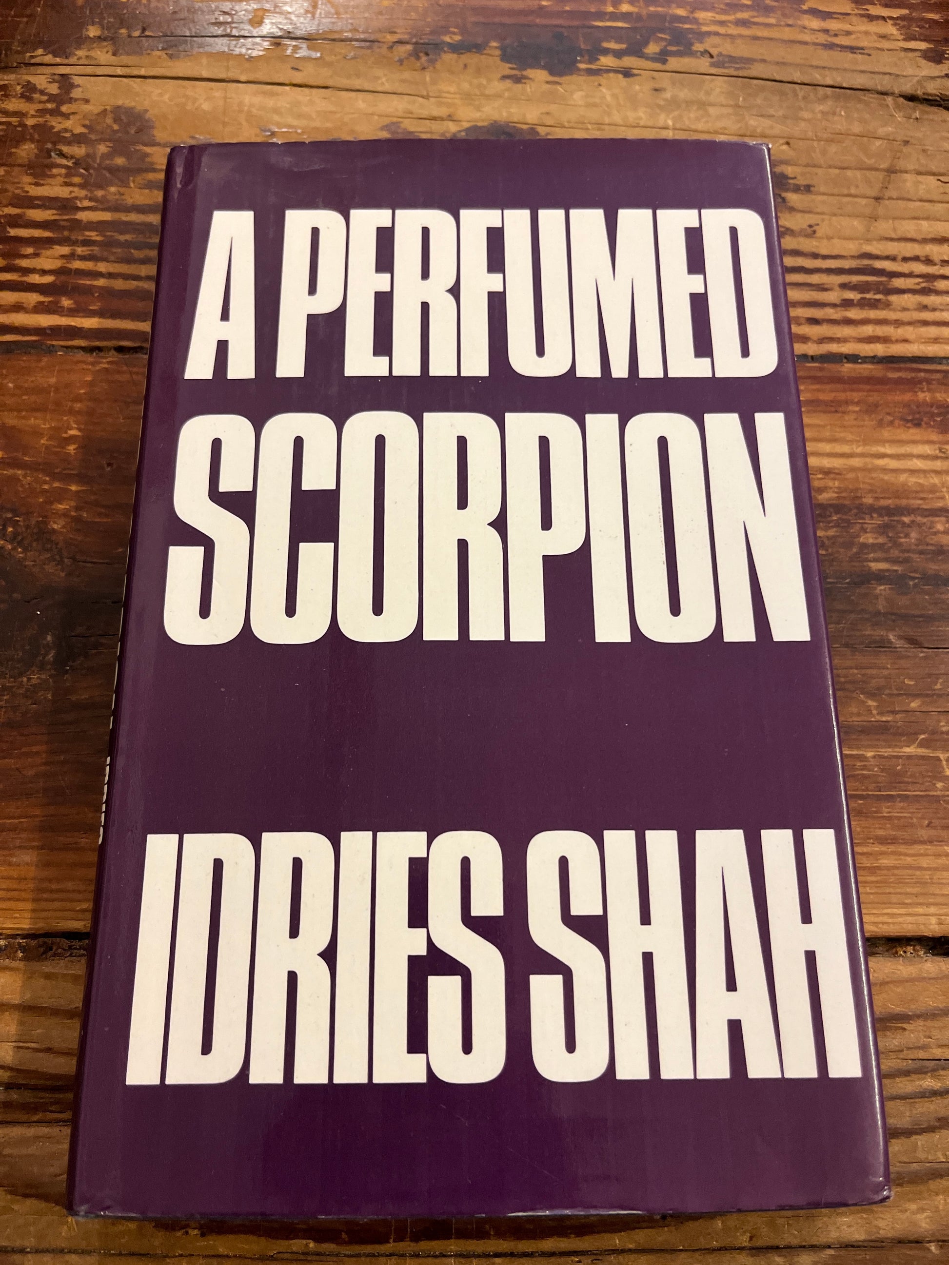 Book titled 'A Perfumed Scorpion' by Idries Shah on a wooden surface