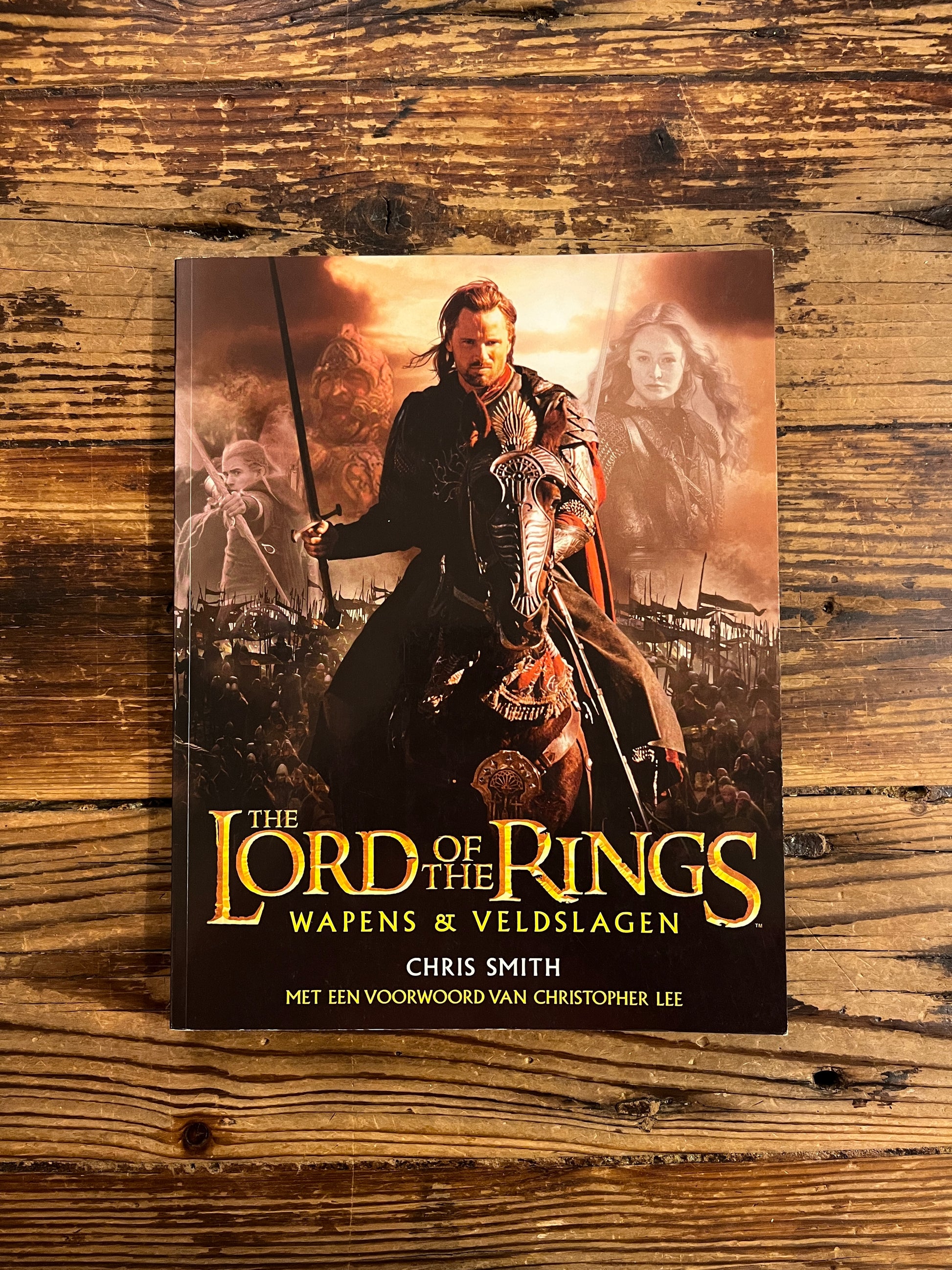 Voorkant van boek met de titel 'the lord of the rings, wapens en veldslagen' op een houten achtergrond 