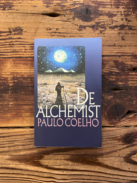 Voorkant van boek met de titel 'de alchemist' door Paulo Coelho op een houten achtergrond 