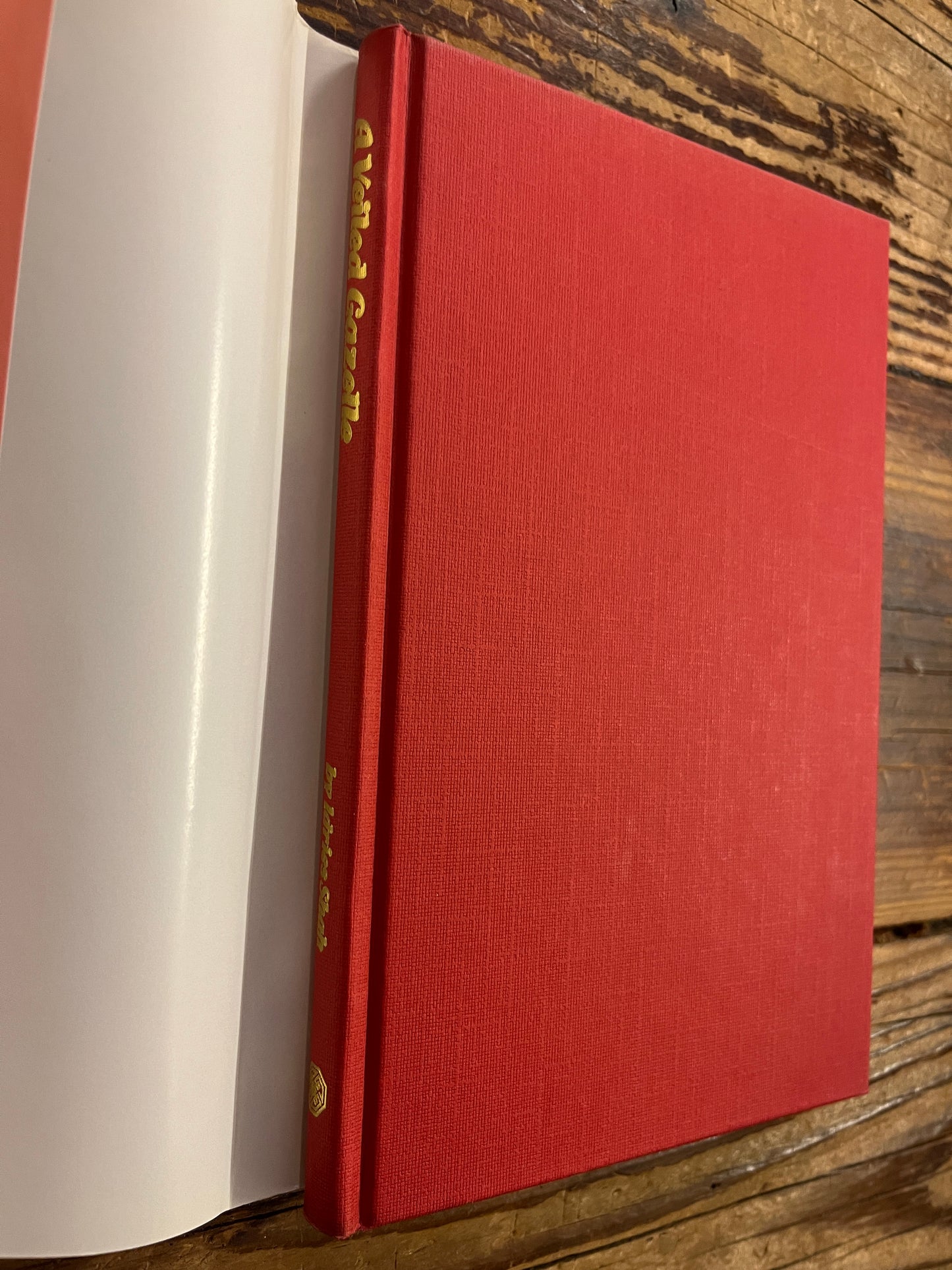 Red book titled 'A Veiled Gazette' by Idries Shah with gold text on a wooden surface