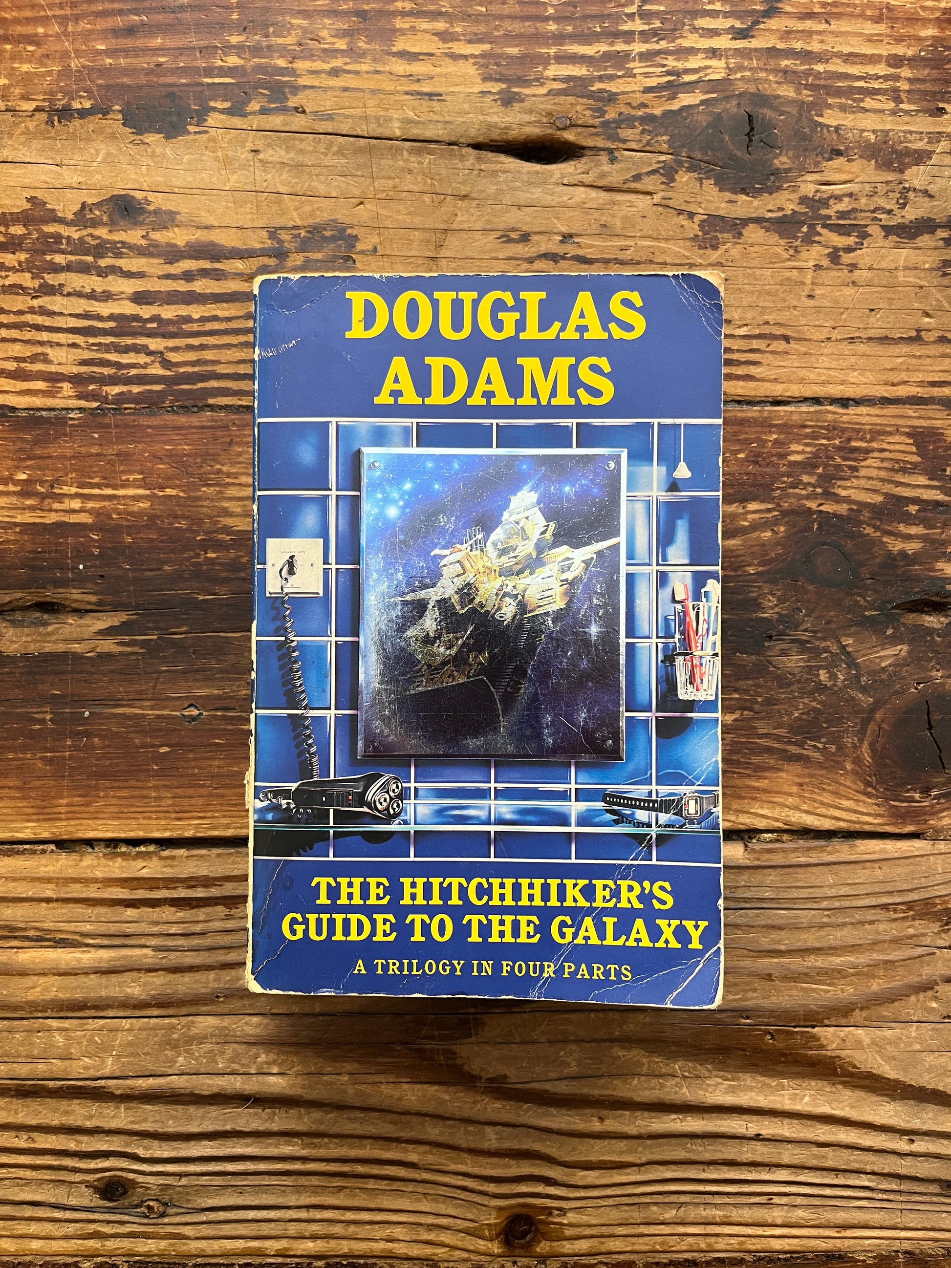 Book cover of 'The Hitchhiker's Guide to the Galaxy' by Douglas Adams on a wooden surface