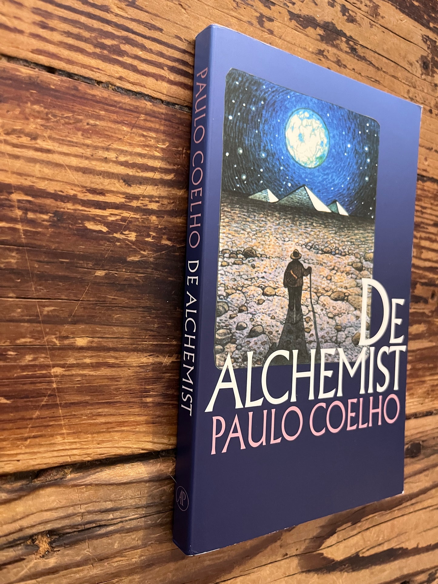 Voorkant en rug van boek met de titel 'de Alchemist' door Paulo Coelho op een houten achtergrond 