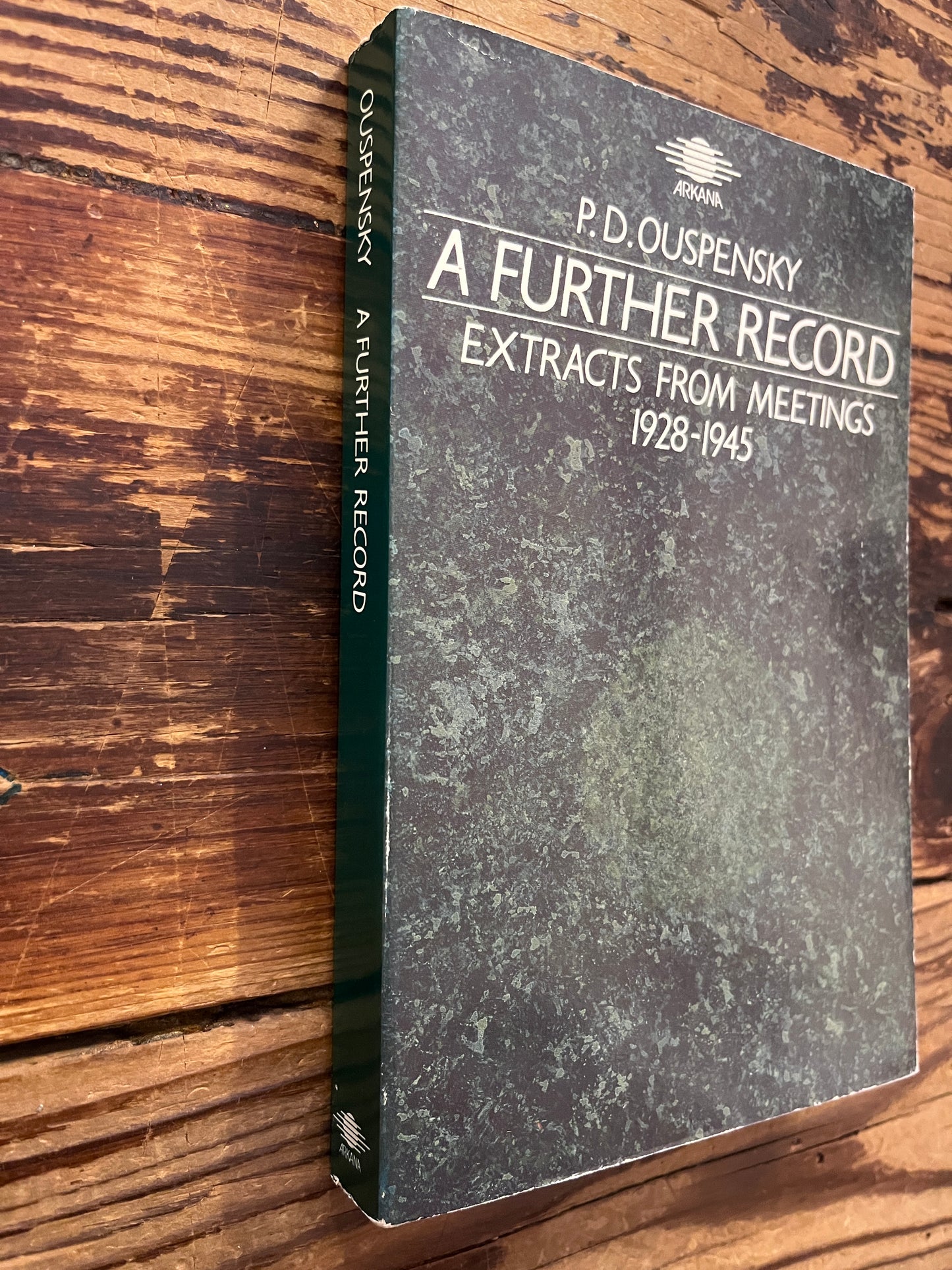 Spine and front cover of a book with the title 'A further record extracts from meetings 1928-1945' by P. D. Ouspensky on a wooden surface