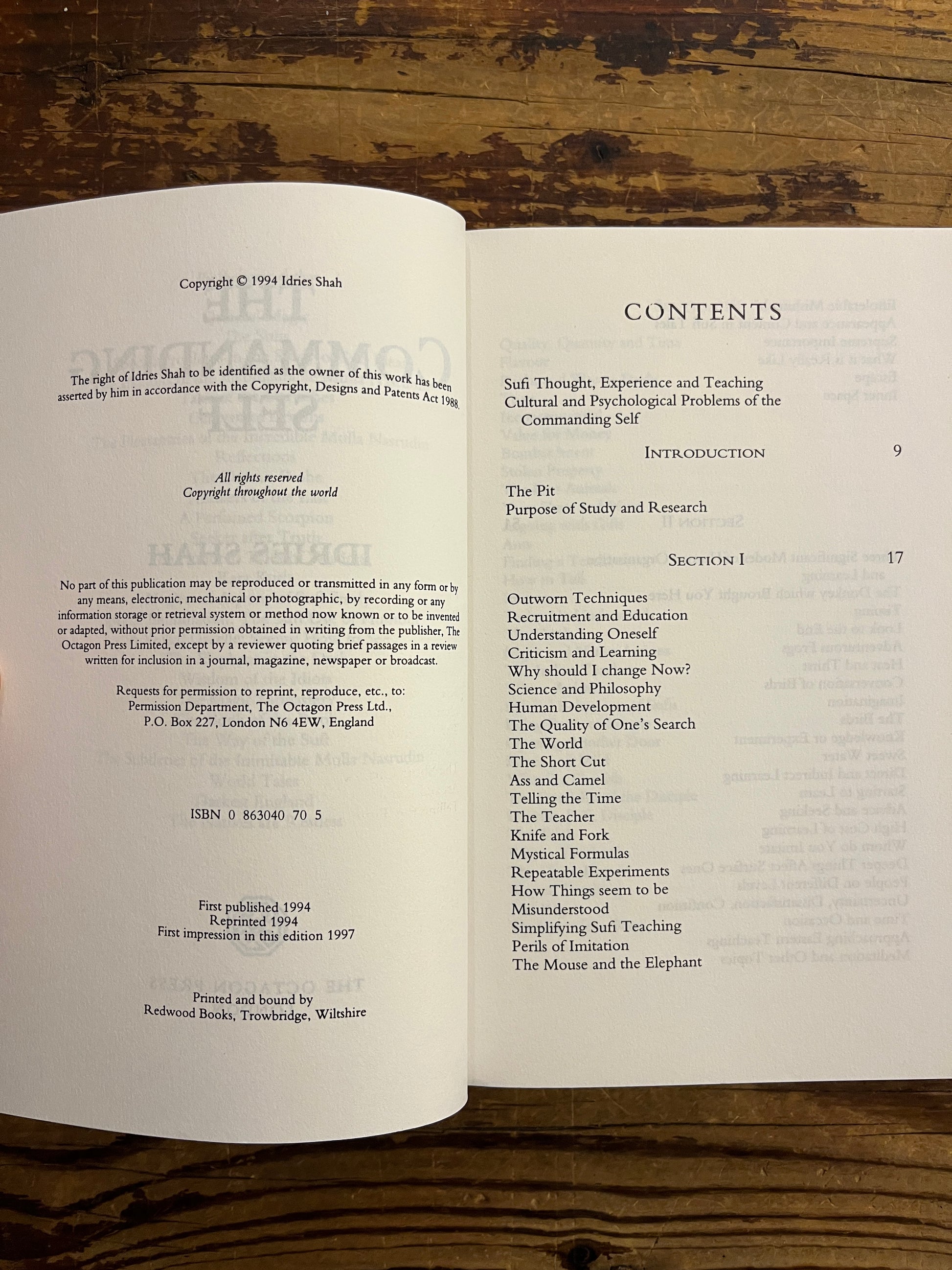 Open book titled 'The Commanding Self' by Idries Shah showing a table of contents on a wooden surface