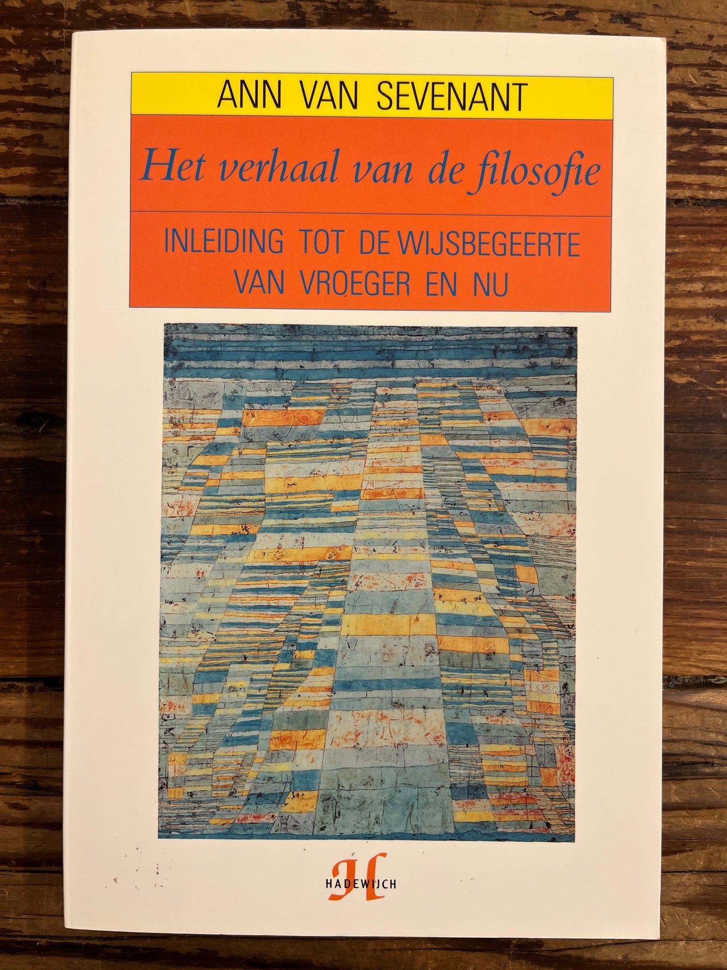 Voorkant van boek met titel 'het verhaal van de filosofie' door Ann van Sevenant op een houten achtergrond 